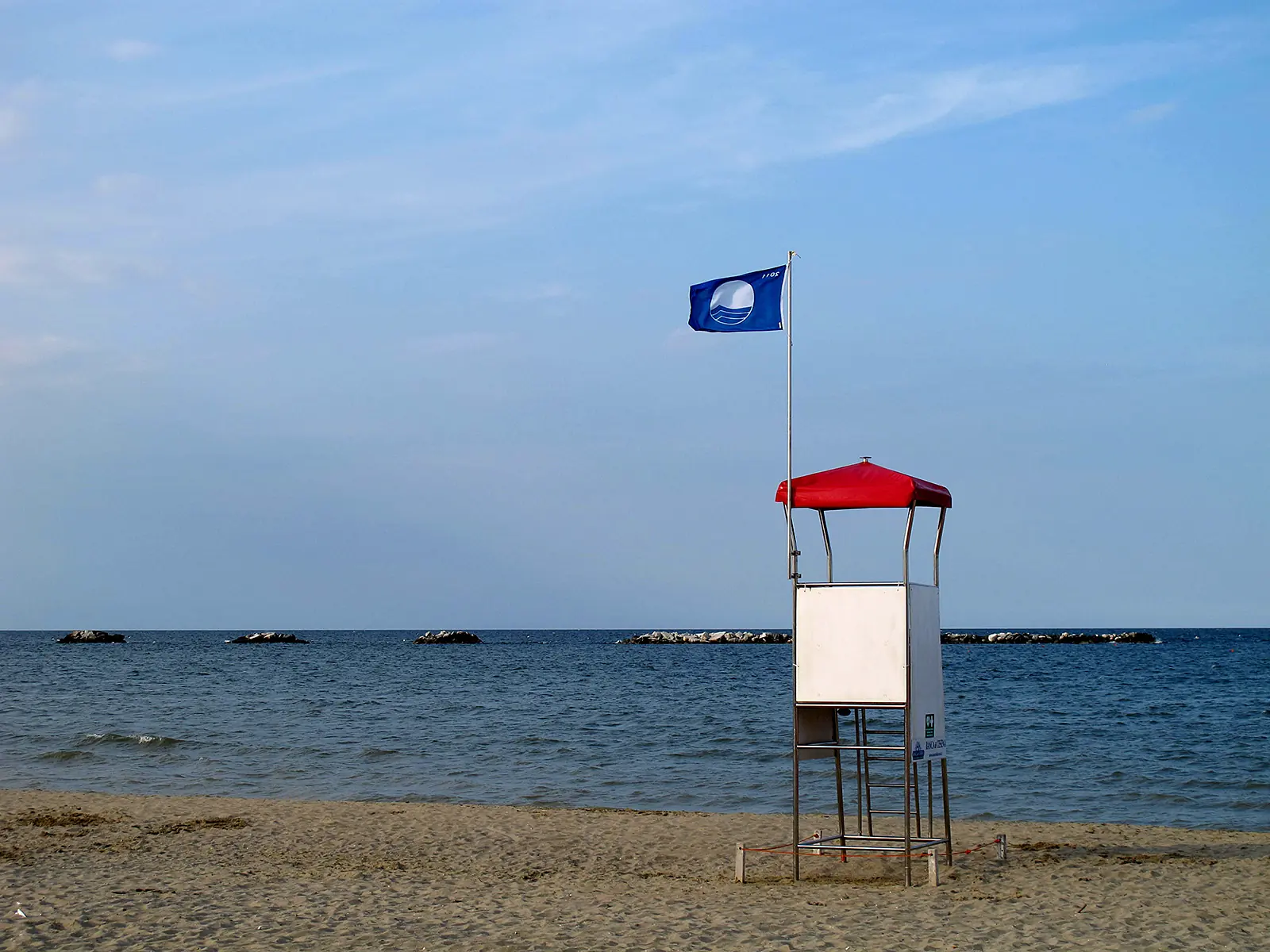 Ein roter Rettungsturm mit wehender blauer Flagge am Strand von Cesenatico, dahinter ruhiges Meer