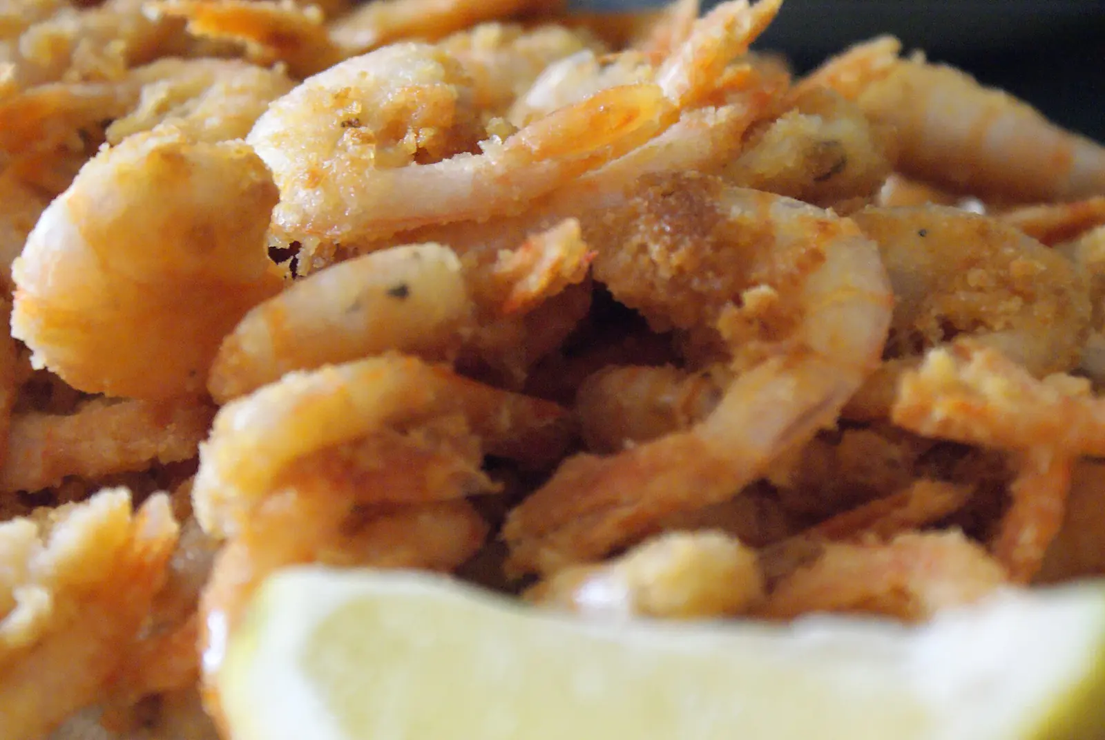 Une assiette de petites crevettes frites et dorées, avec un quartier de citron au premier plan