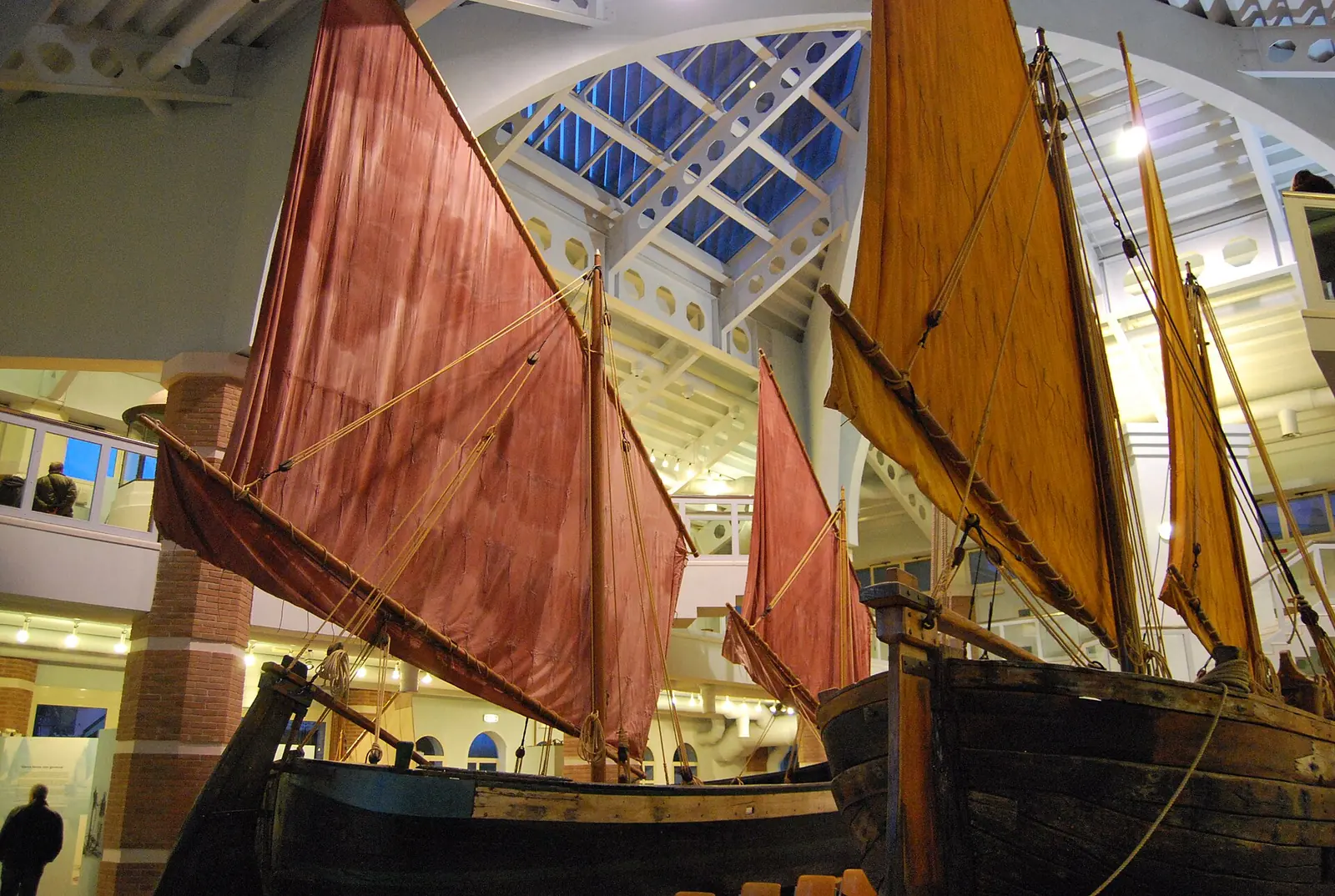 Two traditional boats with red and yellow sails displayed beneath a glass ceiling at Museo della Marineria