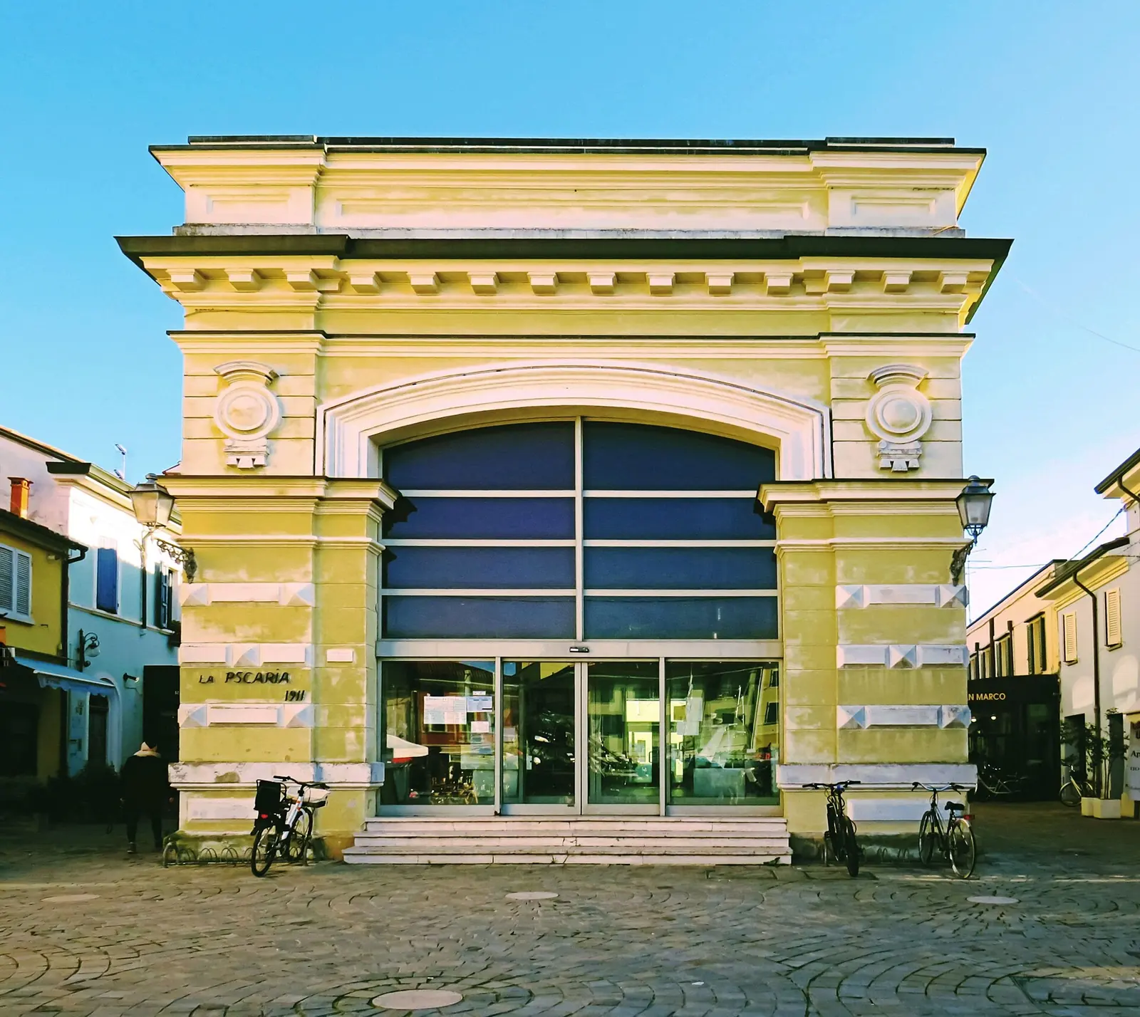 Die gelbe Fassade der Pescheria comunale von Cesenatico mit großem Bogen und Fahrrädern vor dem Eingang