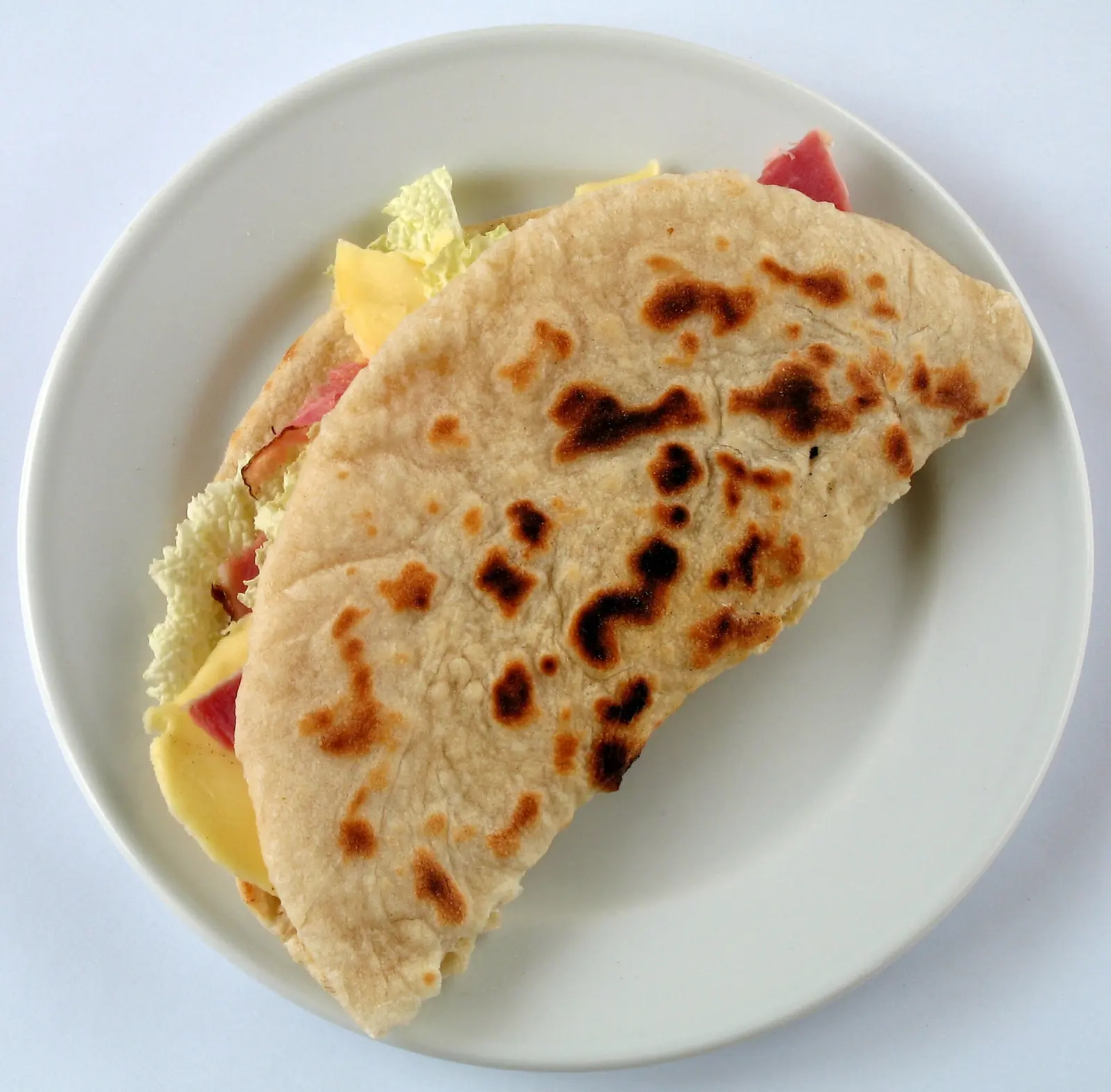 Une piadina pliée et garnie de jambon, de fromage et de salade sur une assiette blanche