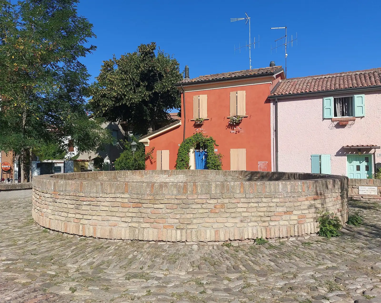 Der runde Eiskeller aus Backstein auf der Piazza delle Conserve mit roten und rosa Häusern und Bäumen im Hintergrund