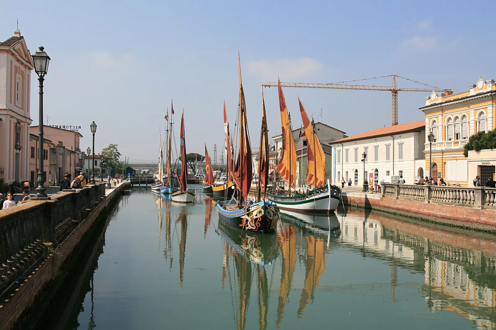 Der Kanalhafen von Cesenatico mit vertäuten traditionellen Segelbooten und Fassaden, die sich im ruhigen Wasser spiegeln