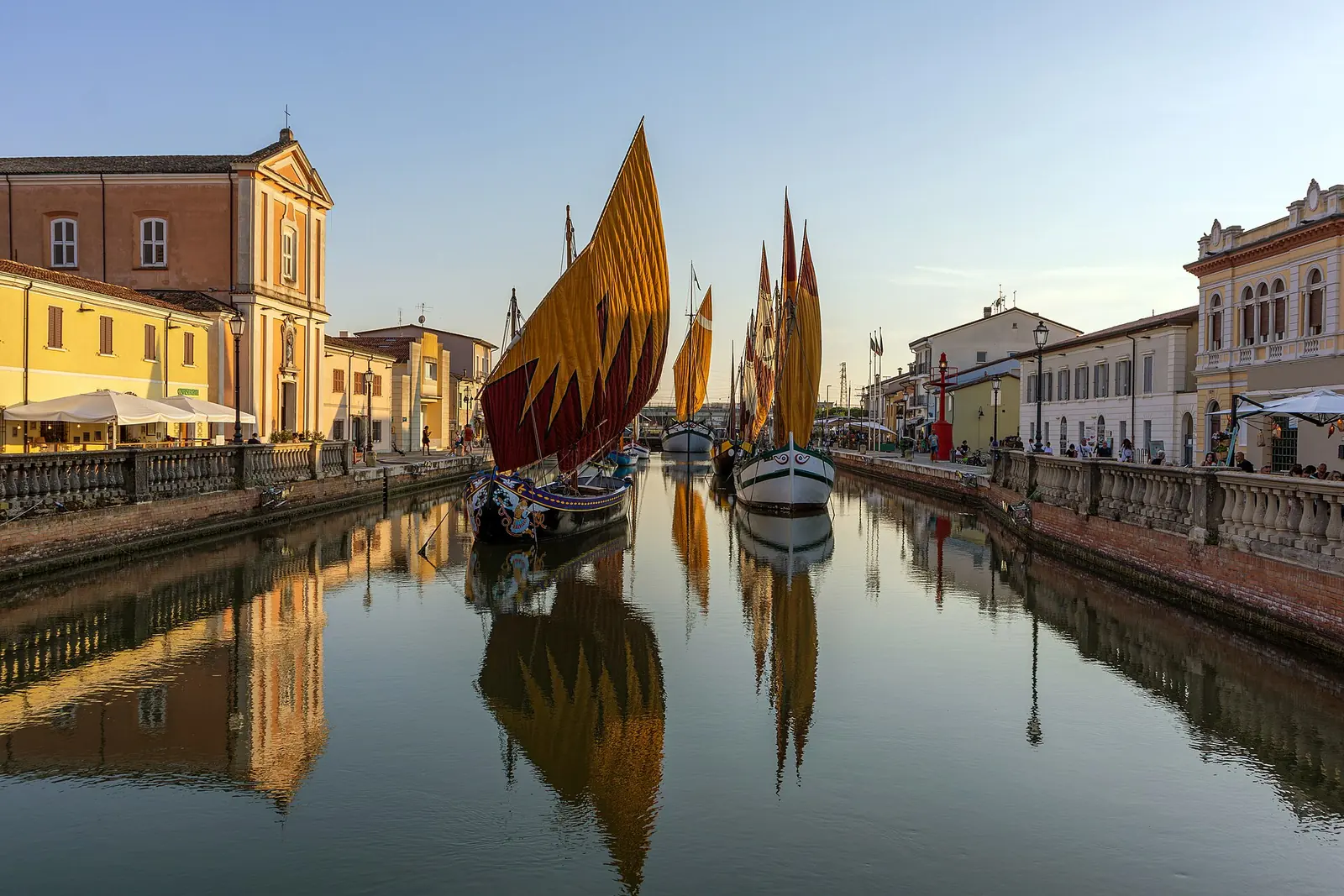 Zwei historische Boote mit gesetzten Segeln im Kanalhafen von Cesenatico mit Spiegelungen der Uferbalustraden im Wasser