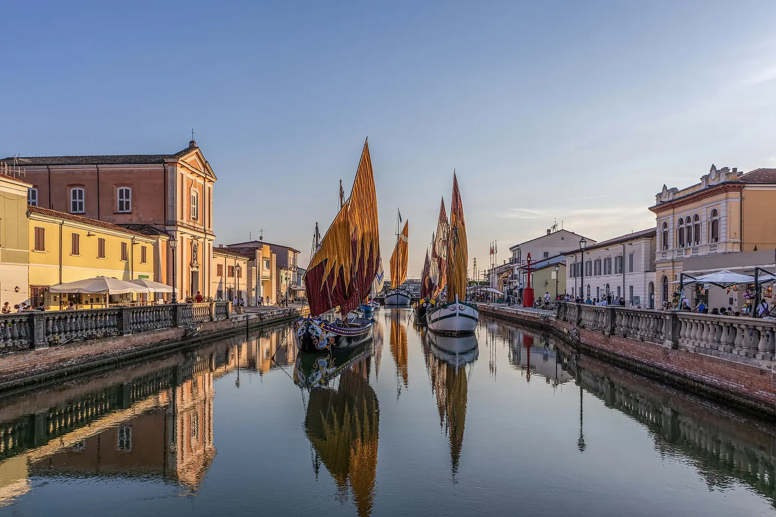 Le barche storiche con le vele gialle e rosse nel porto canale di Cesenatico al tramonto, fra le case della banchina
