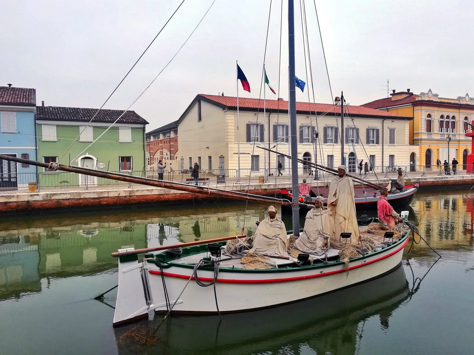 Ein historisches Boot mit Figuren aus hellem Stoff als Krippe auf dem Wasser des Kanalhafens vor den Gebäuden