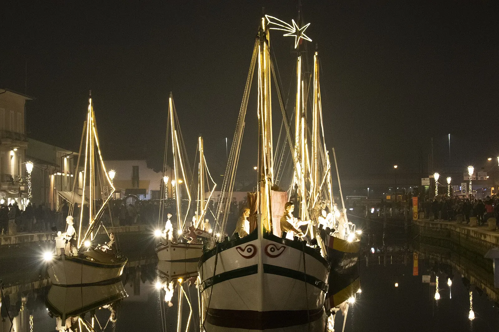 The illuminated historic boats of the floating Nativity scene in Cesenatico's canal harbour in the evening