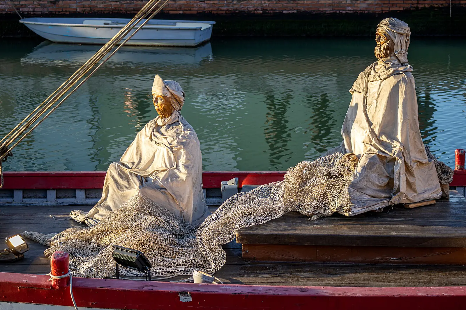 Two statues wrapped in pale drapes and fishing nets on the deck of a floating nativity boat