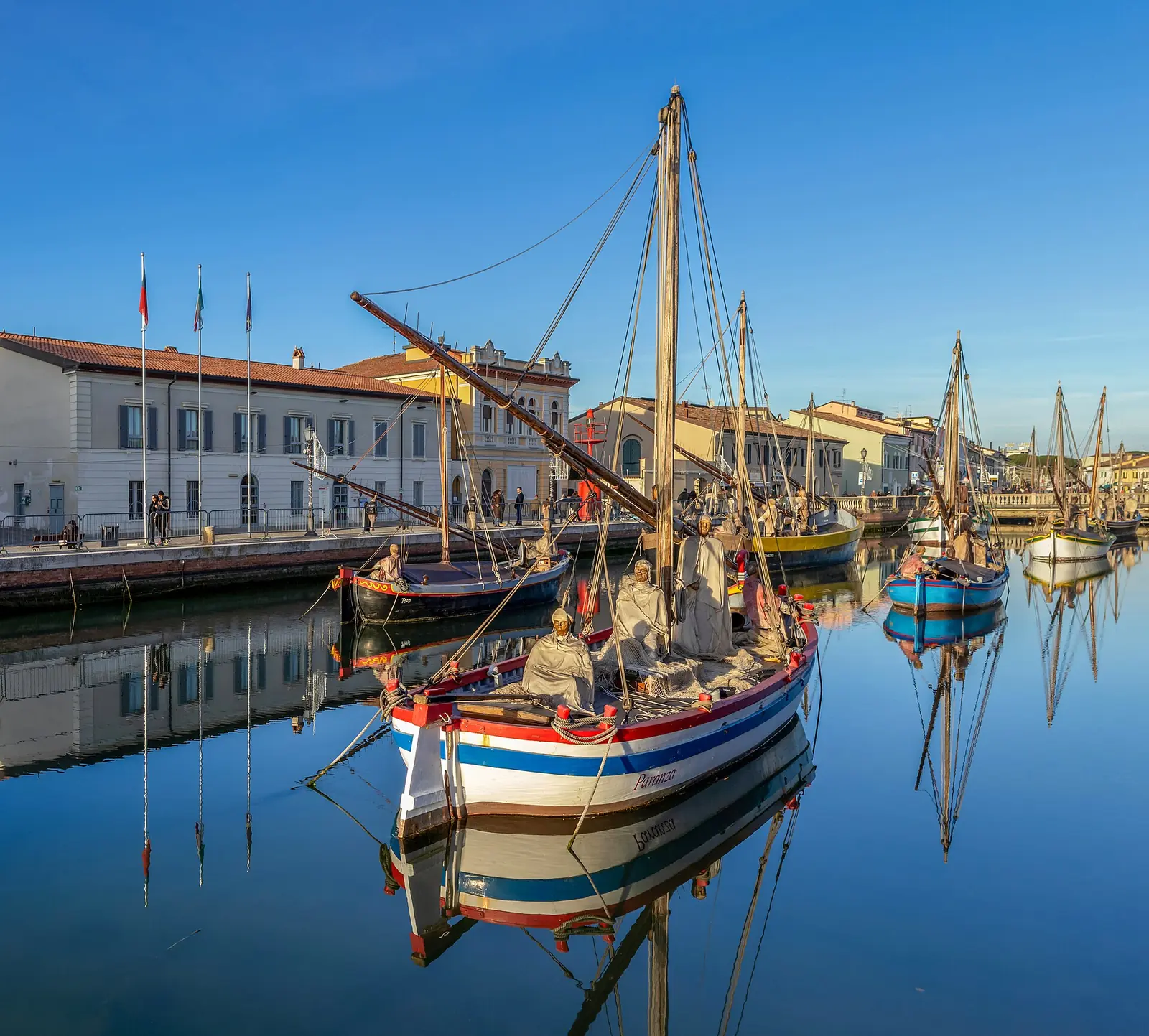 Les statues des Rois mages sur un bateau historique dans le canal de Cesenatico, avec les autres bateaux et les maisons reflétés dans l'eau