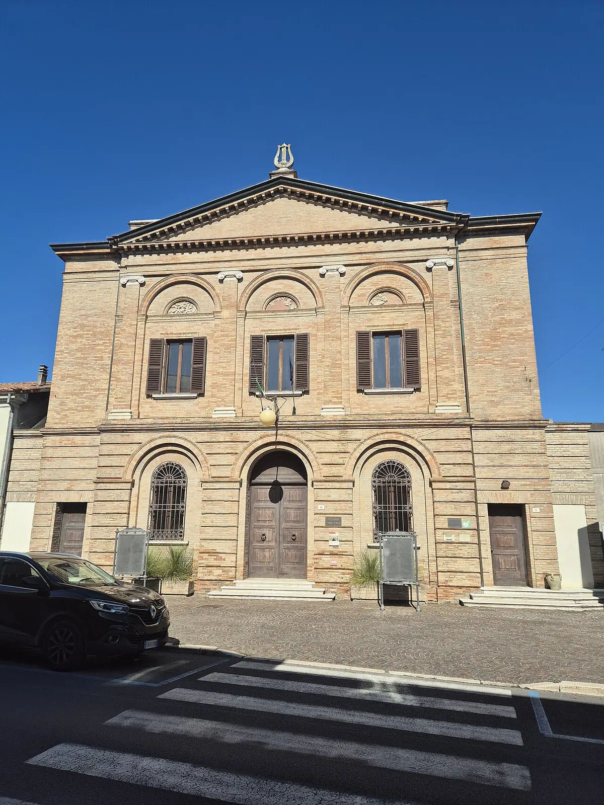 Die neoklassizistische Backsteinfassade des Teatro Comunale von Cesenatico mit drei Fenstern und einem rundbogigen Eingang