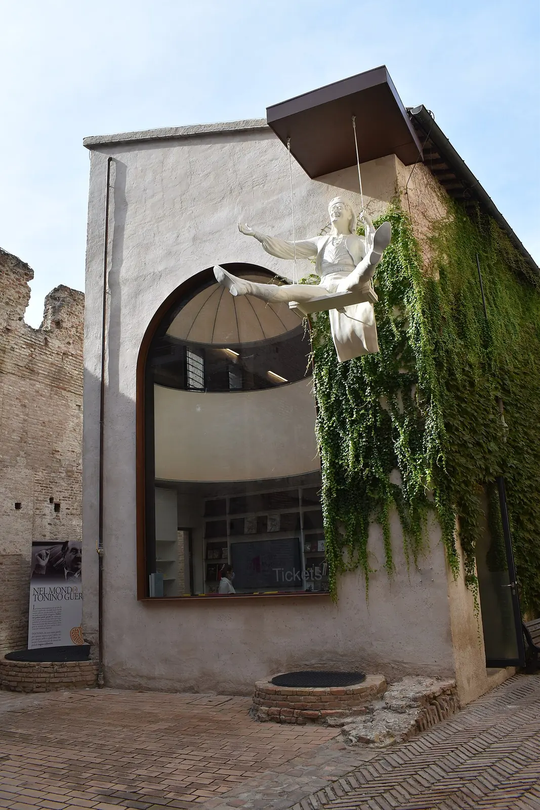 Die Kasse des Fellini Museum in Rimini mit dem großen Bogenfenster und der weißen Skulptur eines Mannes auf einer Schaukel