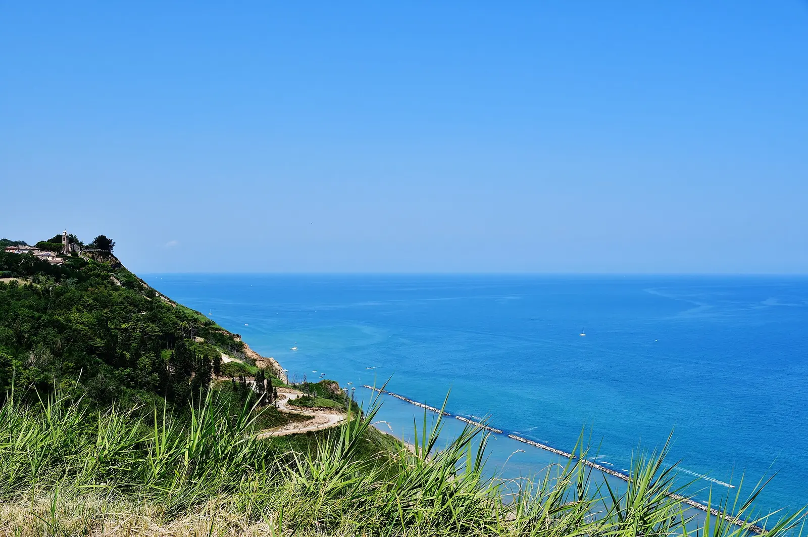 Il borgo di Fiorenzuola di Focara su uno sperone della falesia, sopra il mare azzurro e la strada per la spiaggia