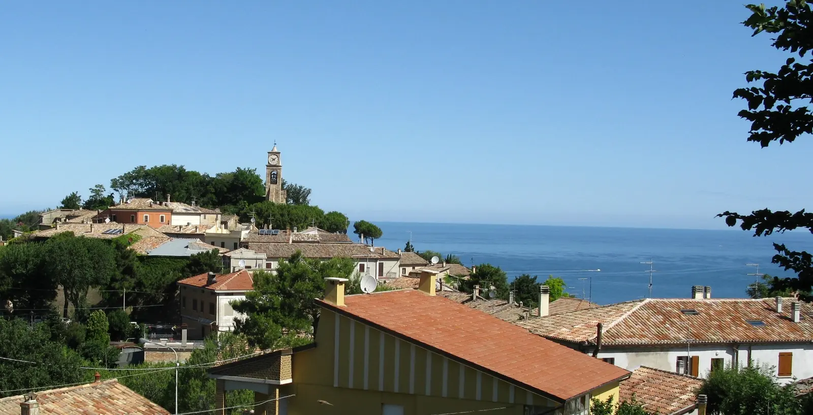 Le case dai tetti di coppi e la torre dell'orologio di Fiorenzuola di Focara, con il mare azzurro sullo sfondo