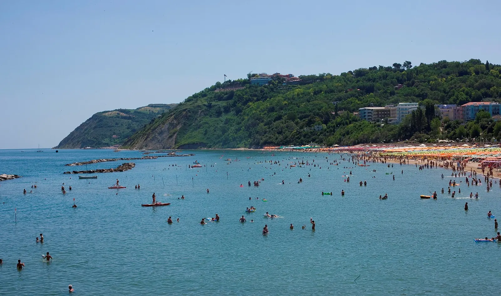 Das grüne Vorgebirge von Gabicce Monte über dem Meer mit dem Strand rechts und entfernten Badegästen