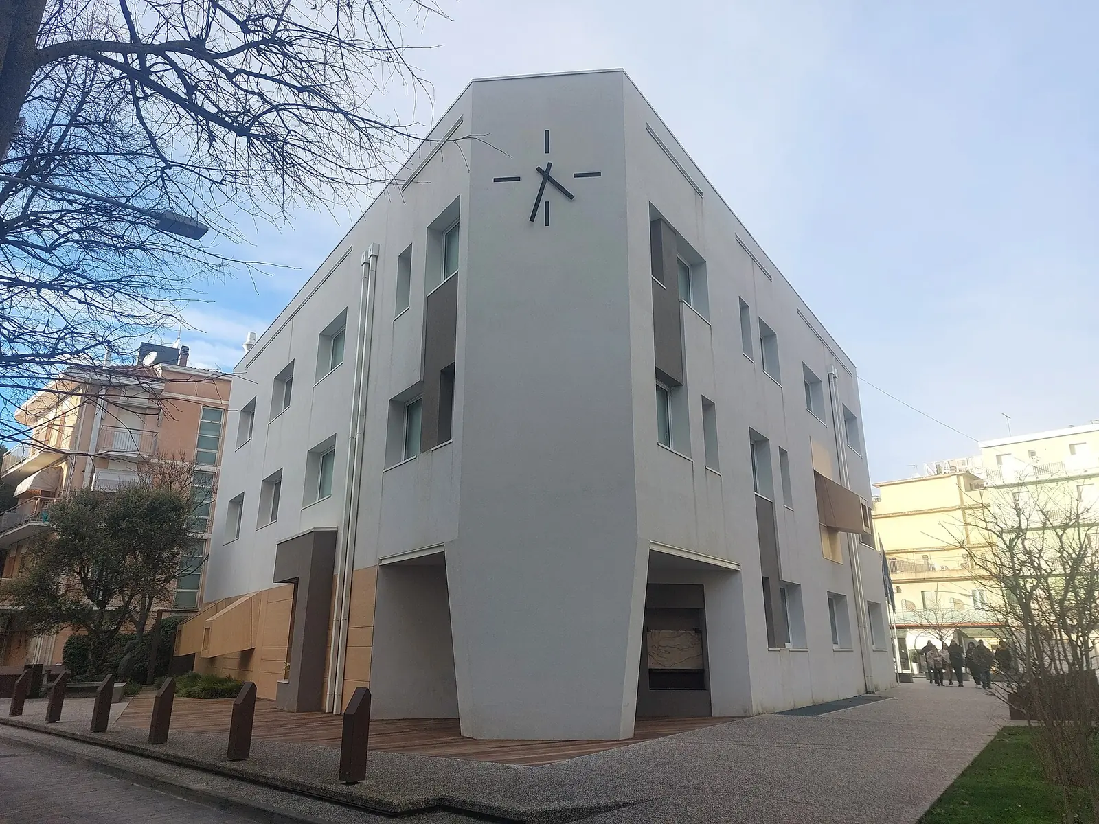 Das Rathaus von Gabicce Mare mit Uhr an der hellen Fassade und einem Fußgängerbereich aus Holz und feinem Kies davor