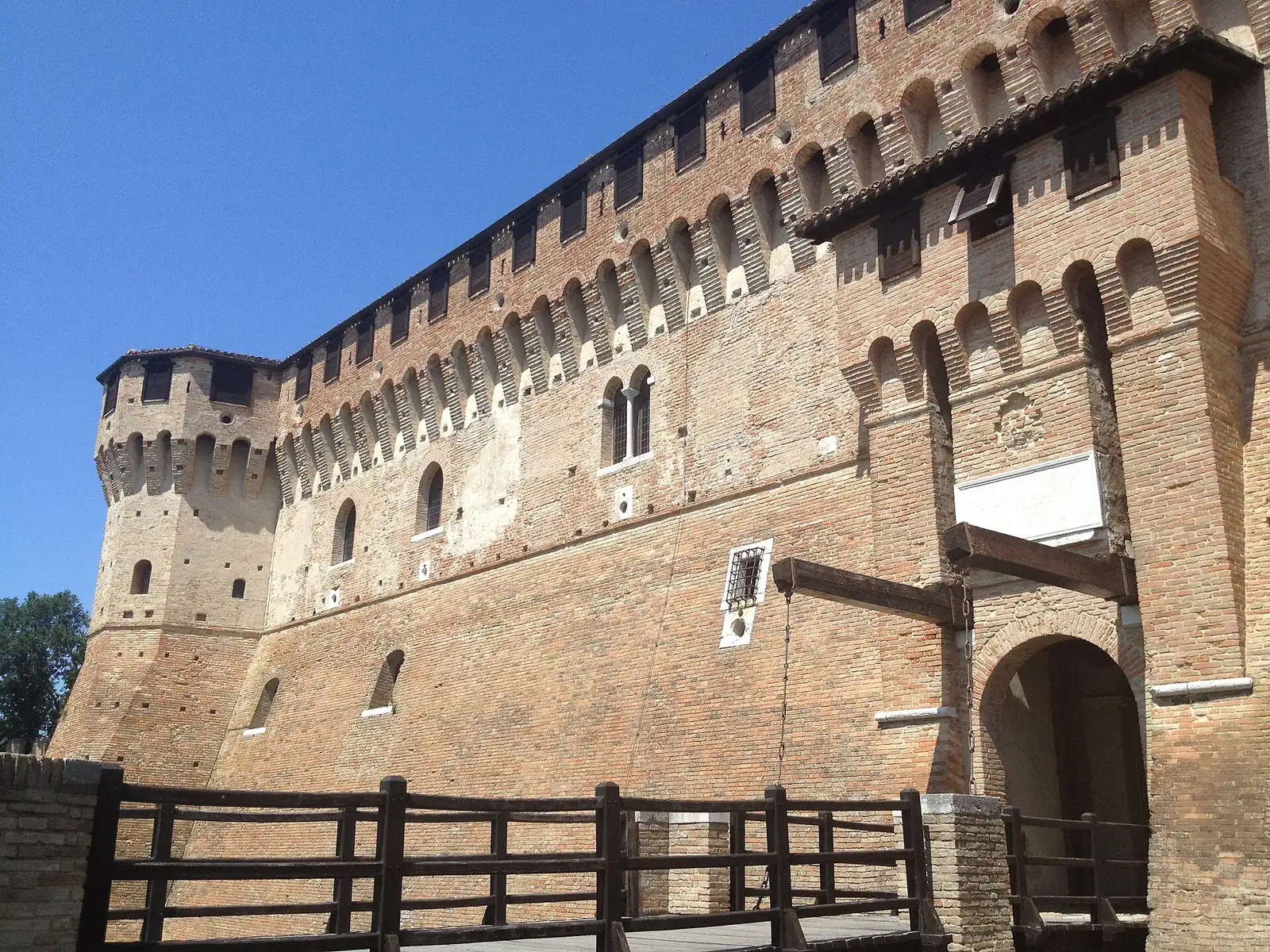 La parete in mattoni della Rocca di Gradara con le merlature, il portale e il ponte levatoio in legno in primo piano