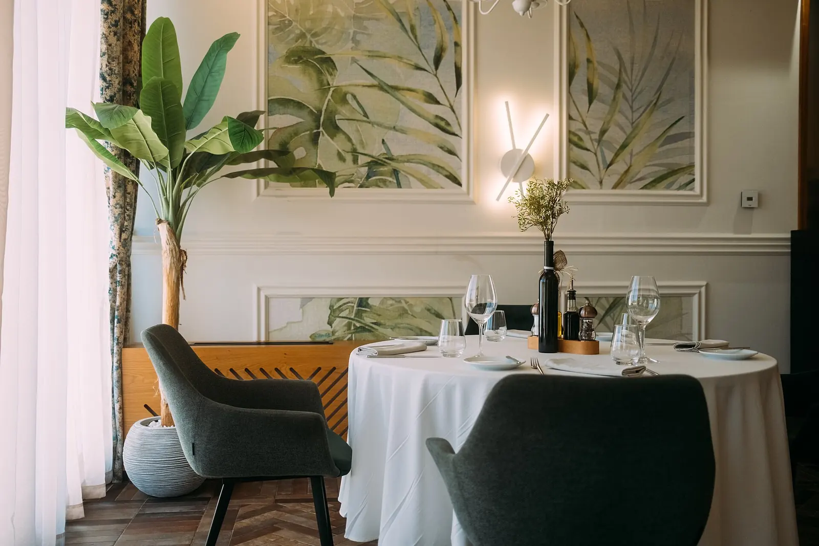 A hotel dining room with a set round table, a white tablecloth and two grey armchairs