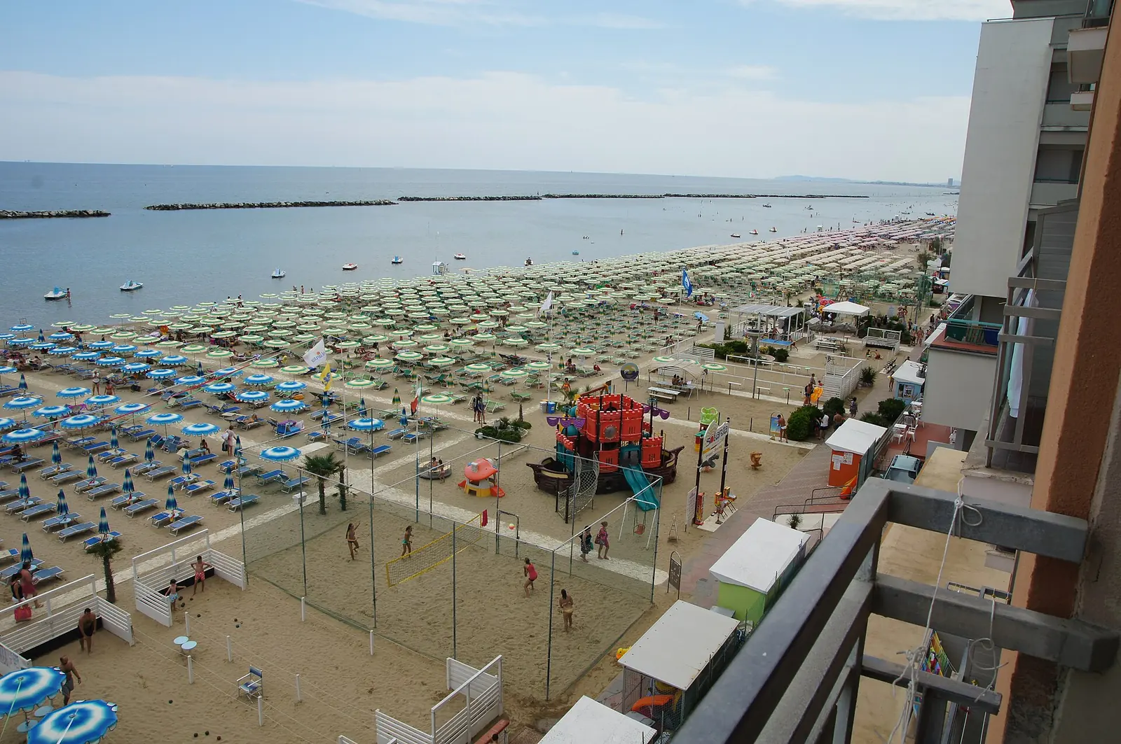 Der Strand von Igea Marina von oben, mit einem Beachvolleyballfeld, einer Spielburg für Kinder und Sonnenschirmreihen
