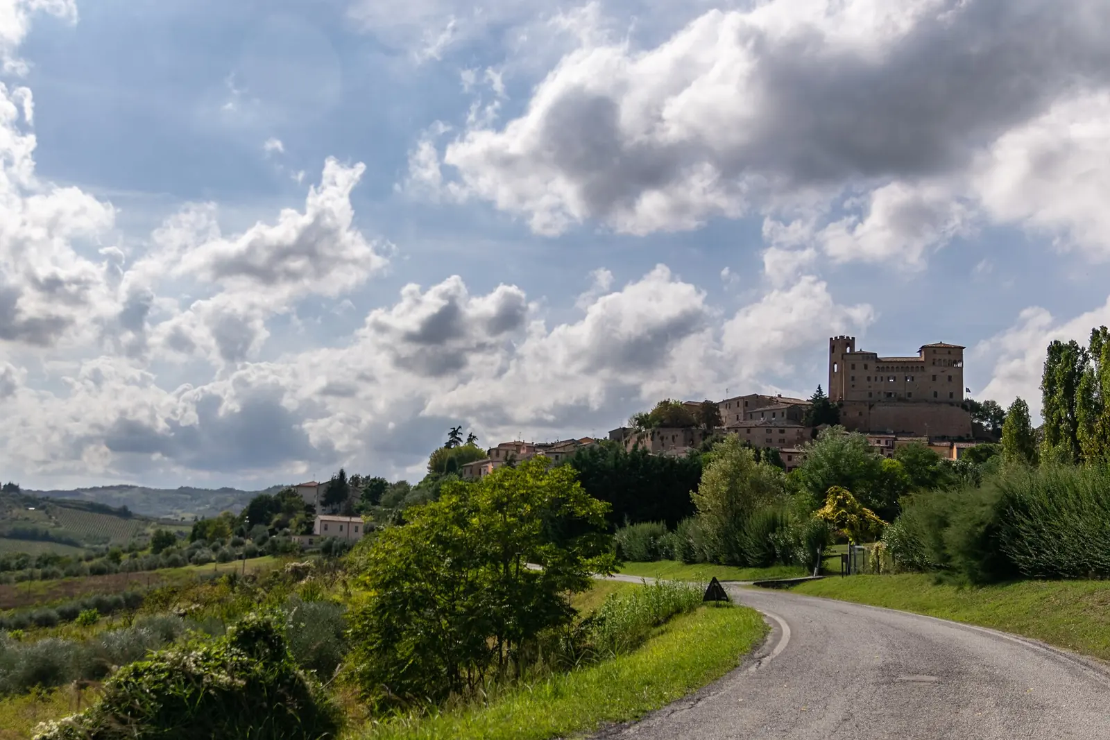 Das Castello Malatestiano di Longiano auf dem Hügel mit einer Straße durch die Vegetation hinauf zur Burg und Wolken am Himmel