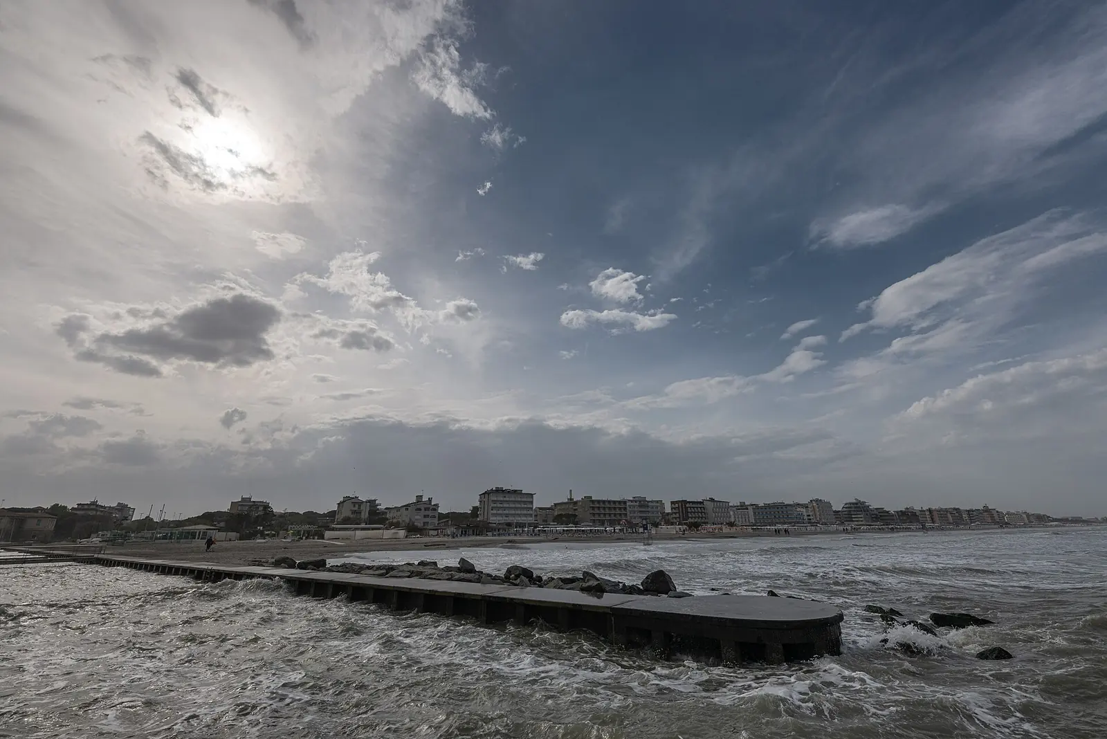 Waves battering the Canalino pier, with Milano Marittima's beach and buildings in the distance