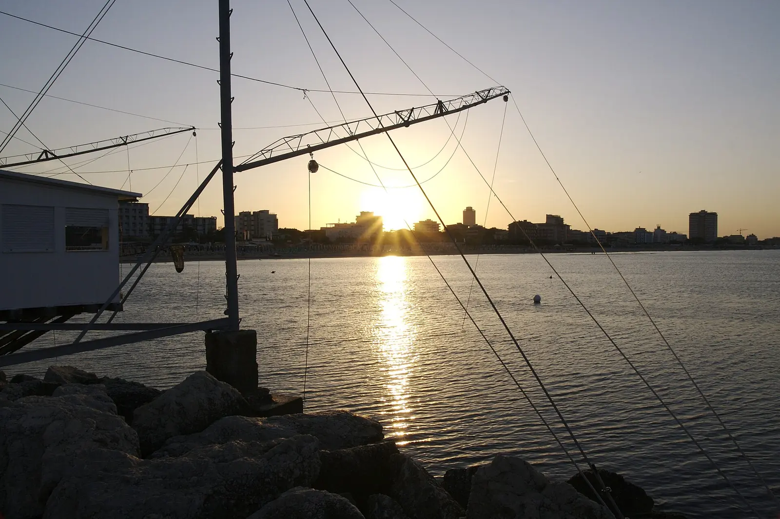 Il sole al tramonto dietro un capanno da pesca sul molo, con il profilo delle case di Milano Marittima in lontananza