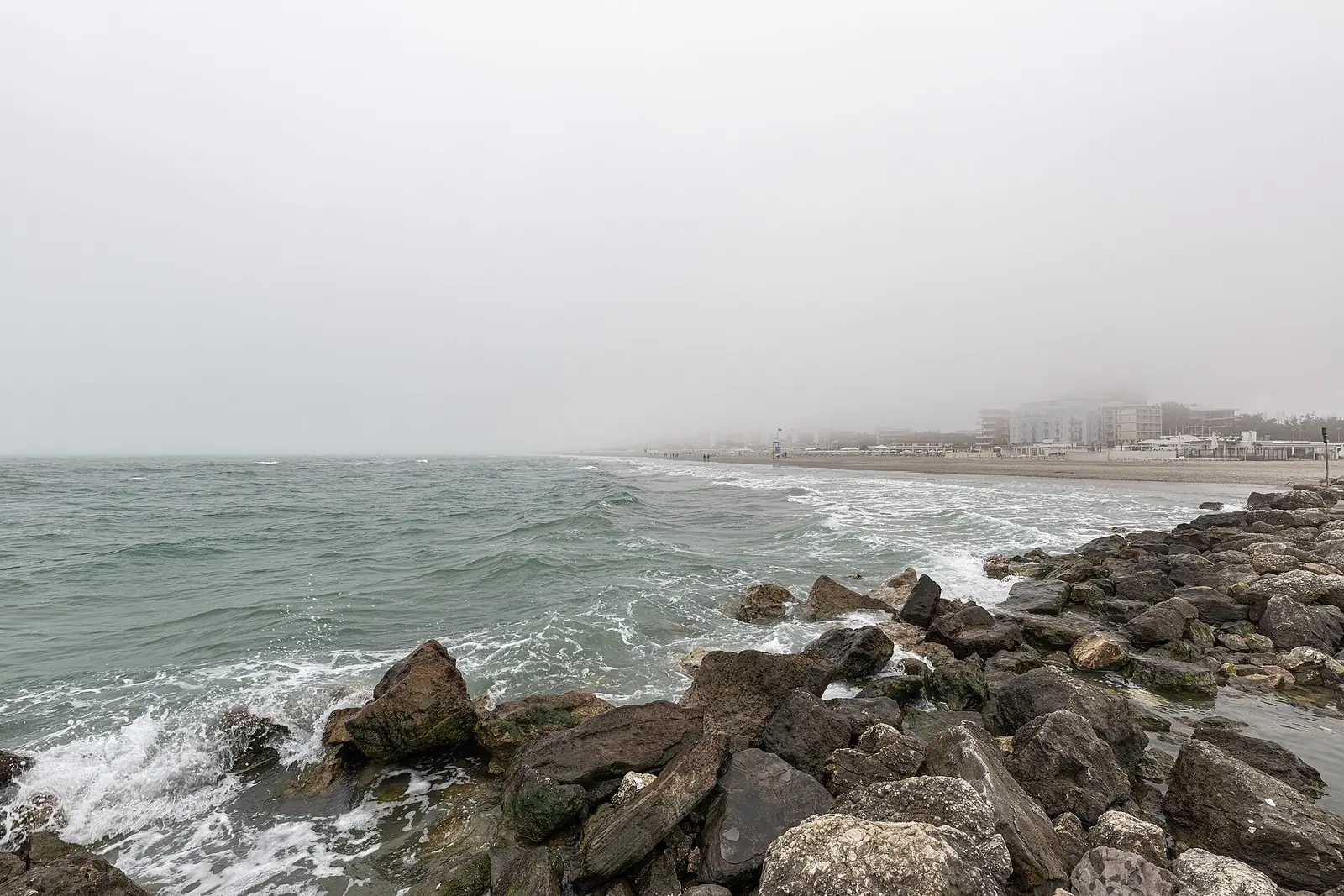 Breakwaters and waves on the Milano Marittima coast, with the beach and buildings fading into the haze
