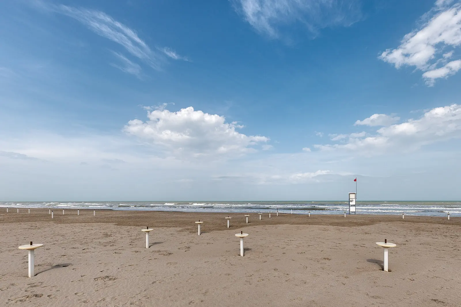 La spiaggia di Milano Marittima in primavera, con le basi degli ombrelloni sulla sabbia, una torretta e il cielo azzurro