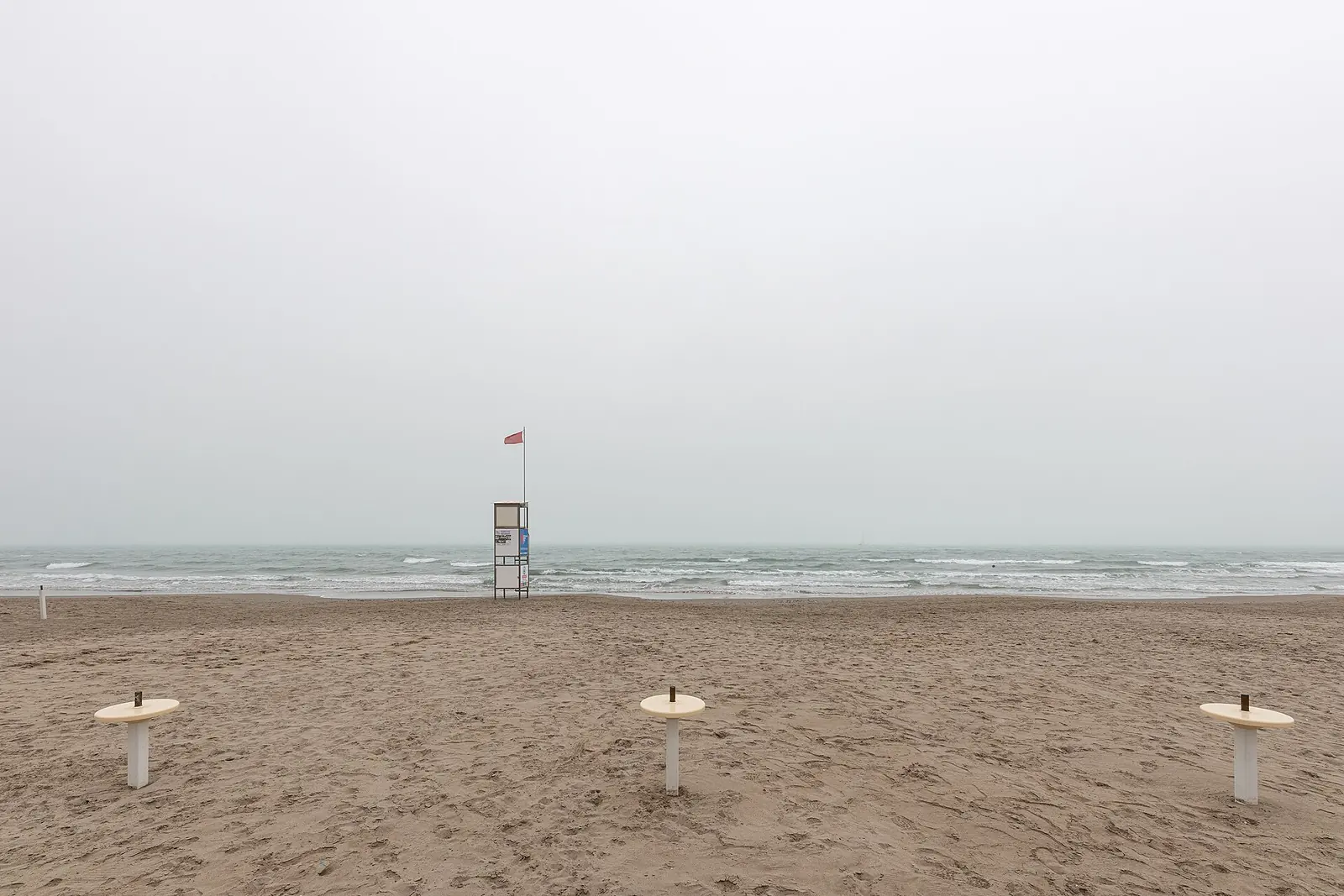 Una torretta di salvataggio con la bandiera rossa davanti al mare increspato, in una giornata di foschia