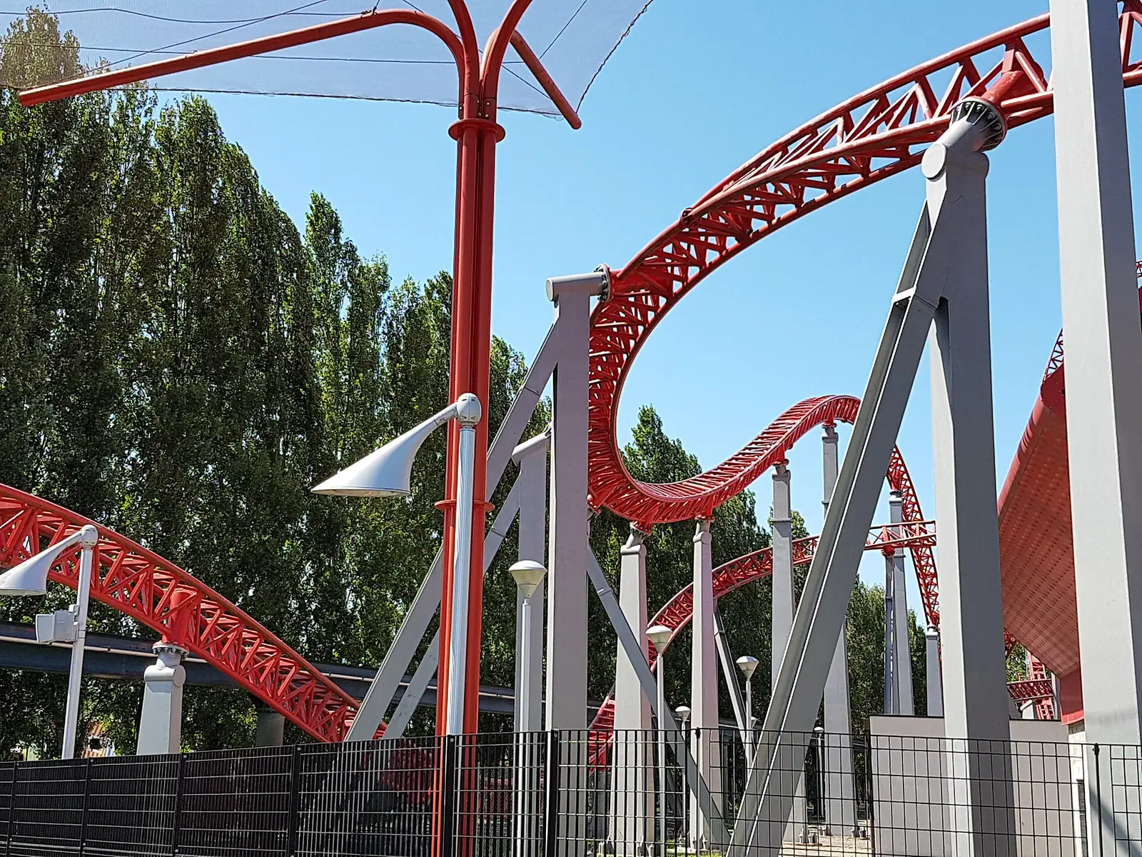 Le travi rosse e grigie del tracciato delle montagne russe iSpeed, con gli alberi del parco dietro la recinzione