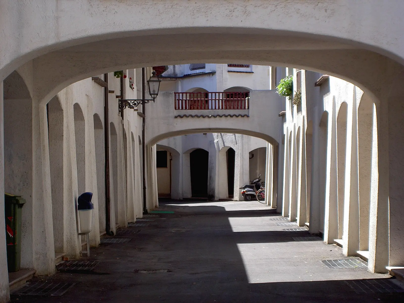 An arched passage between white buildings in Portoverde, with a red balcony in the background and a parked scooter