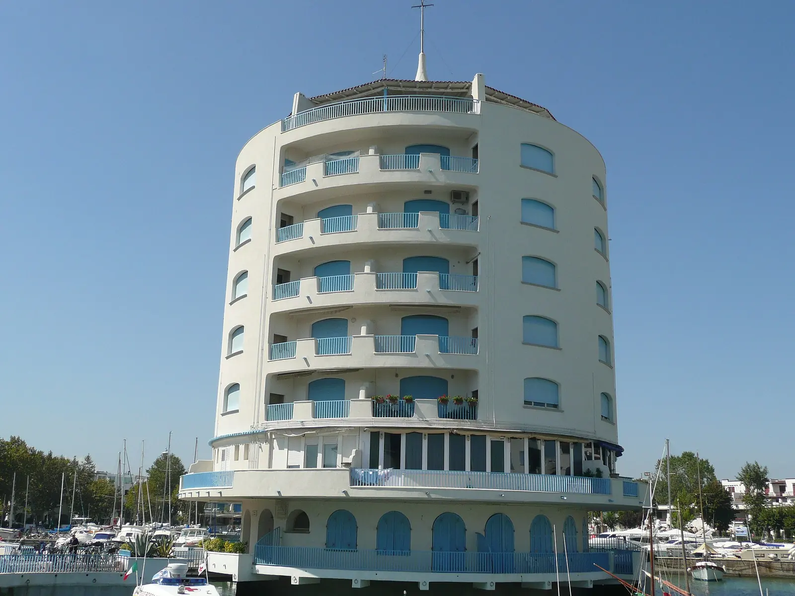 Der weiße Rundturm mit blauen Balkonen über dem Hafenbecken von Portoverde