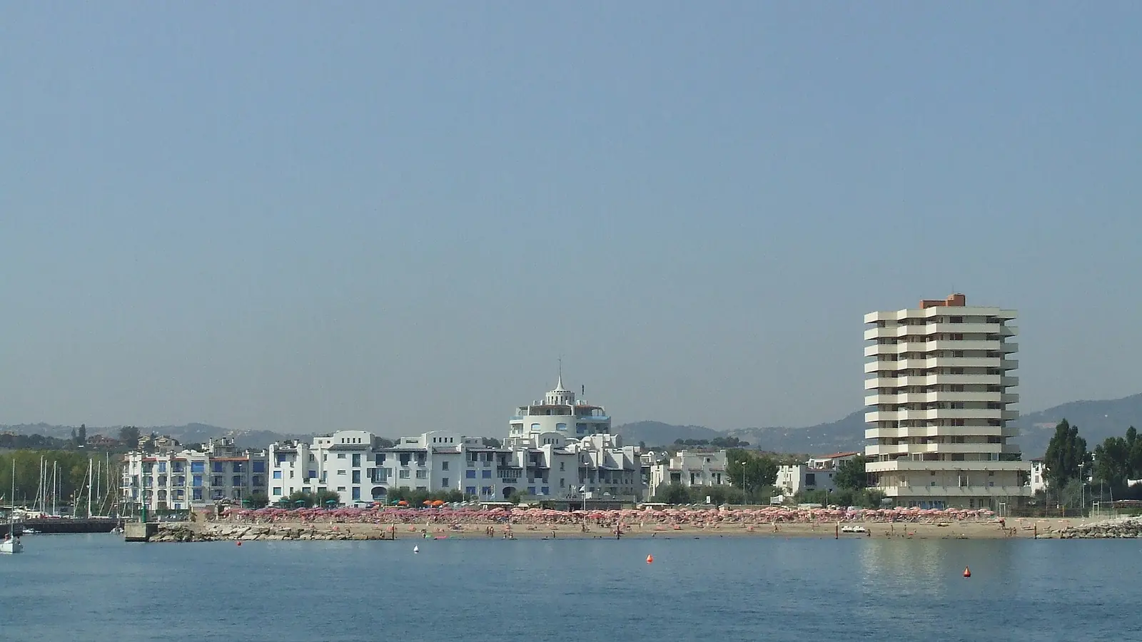 Portoverde vom Meer aus mit weißen Gebäuden am Strandrand und einem Wohnhochhaus rechts
