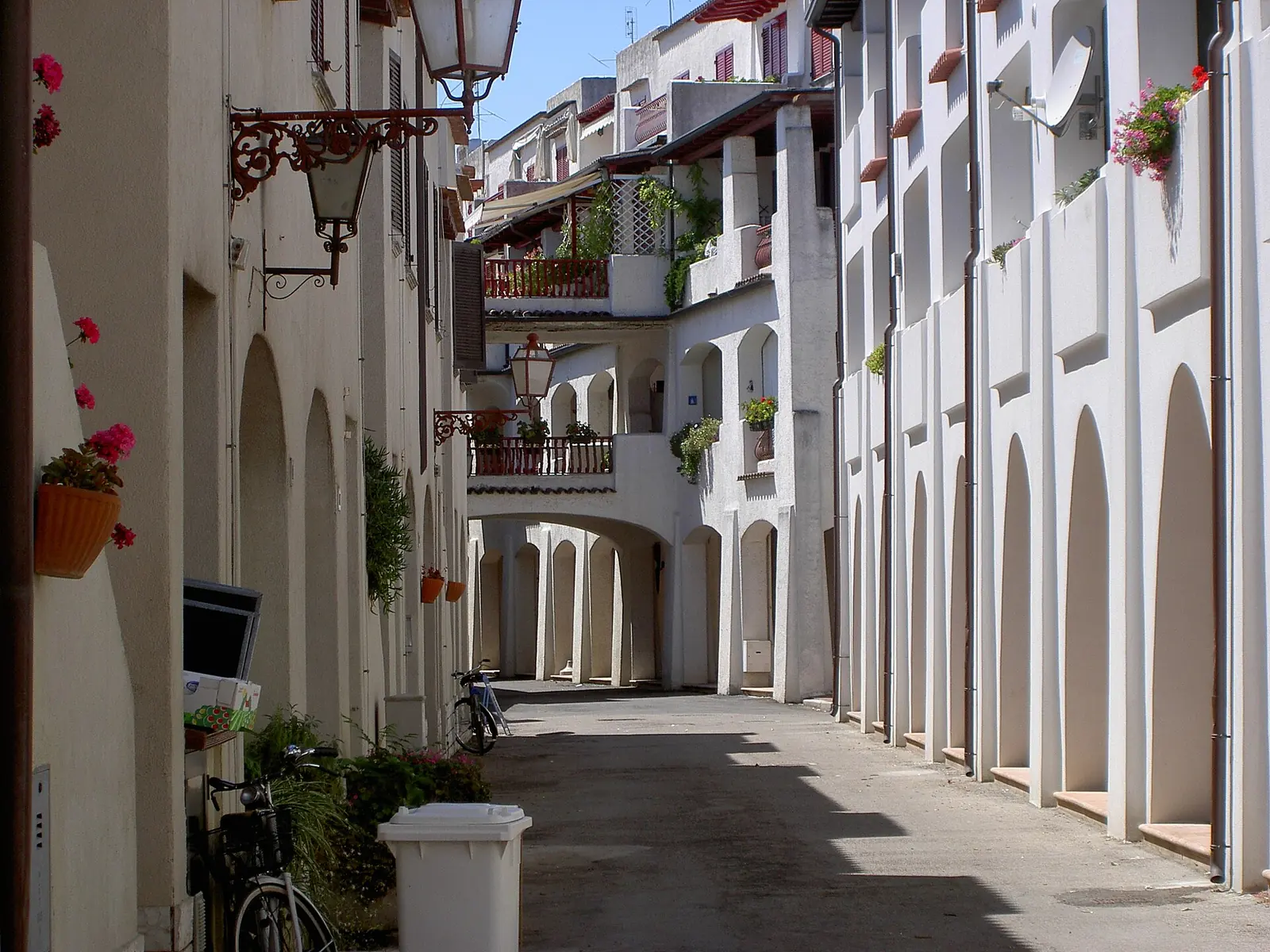 A Portoverde alley with arched porticoes, flower-filled balconies, wrought-iron street lamps and bicycles leaning against the wall