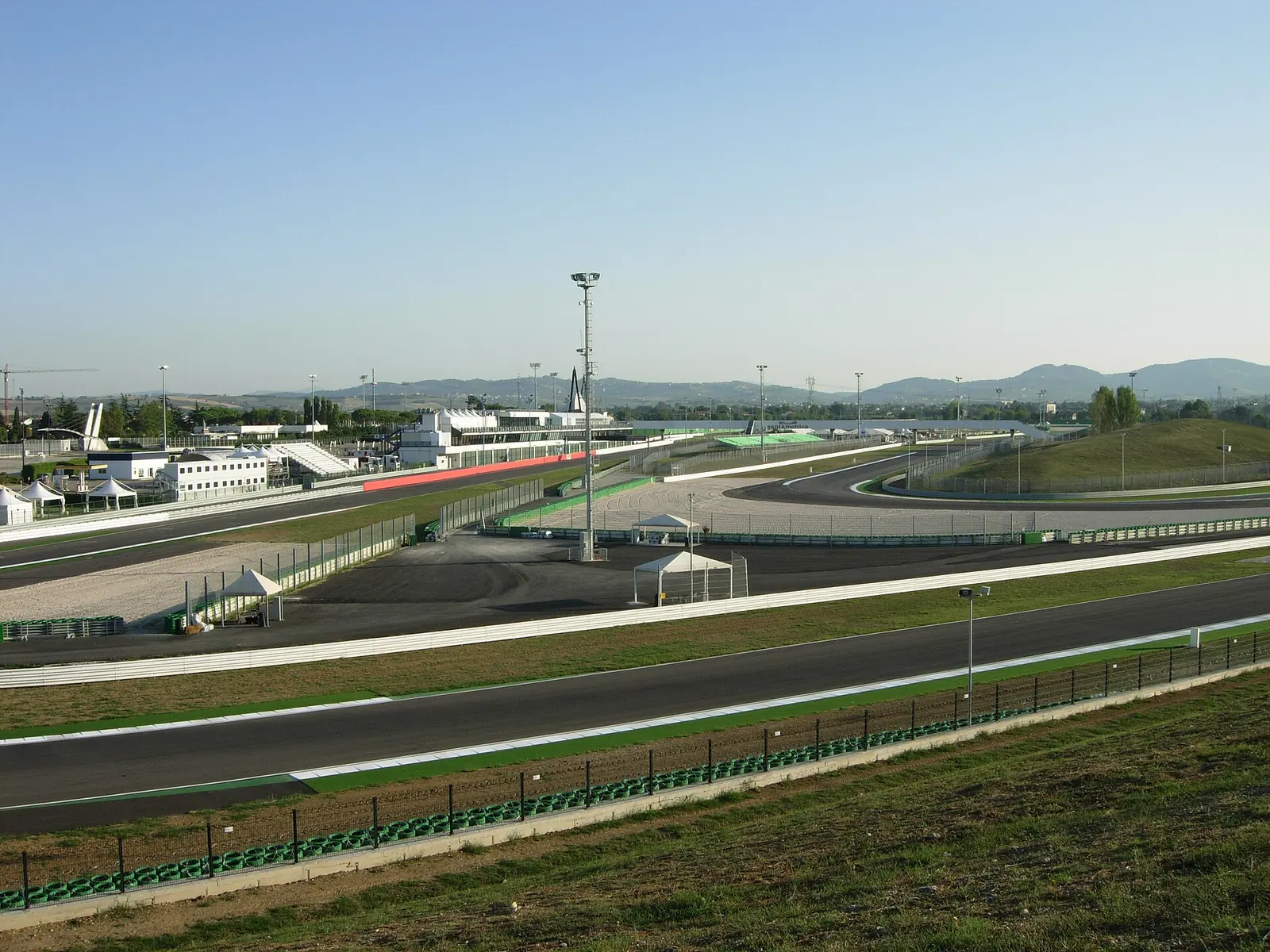 Die Strecke des Misano World Circuit von einem kleinen Hügel aus gesehen, mit Boxen und weißem Turm hinter der Kurve