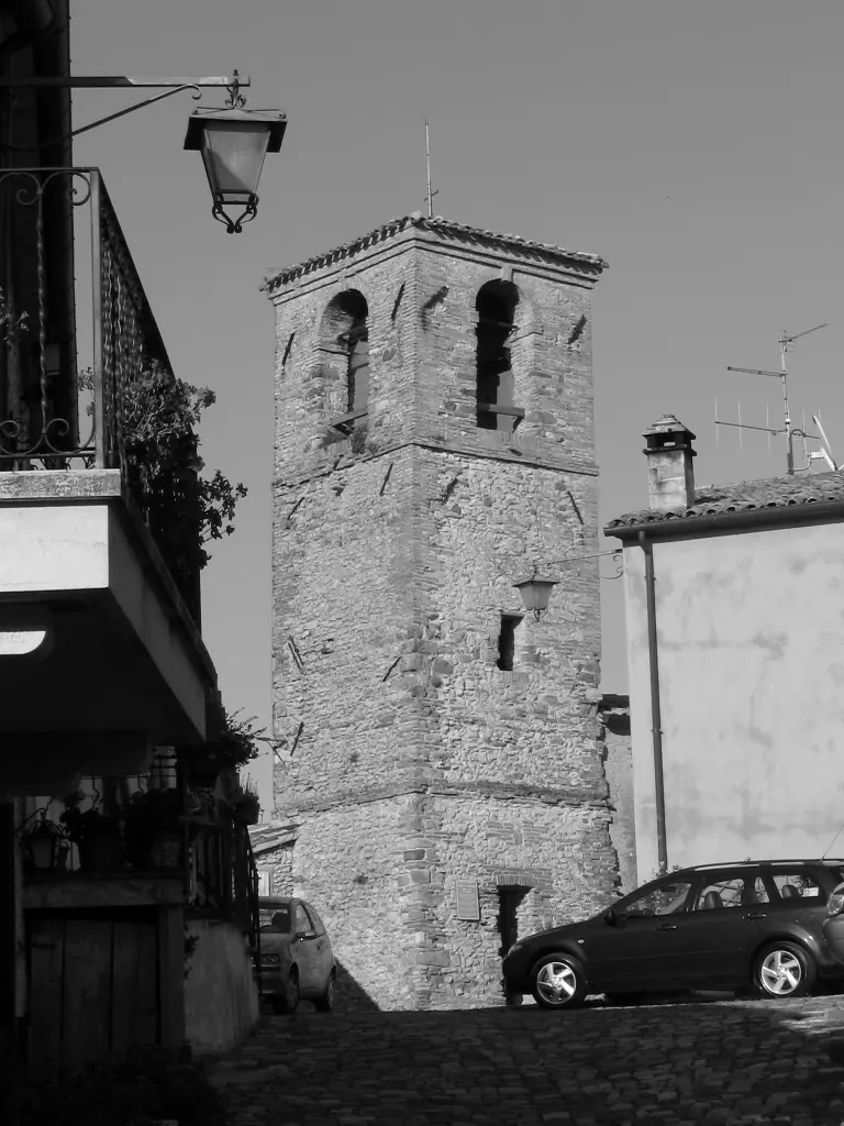 La torre in pietra del borgo di Montebello, con due aperture ad arco in cima, in fondo a una strada lastricata fra le case