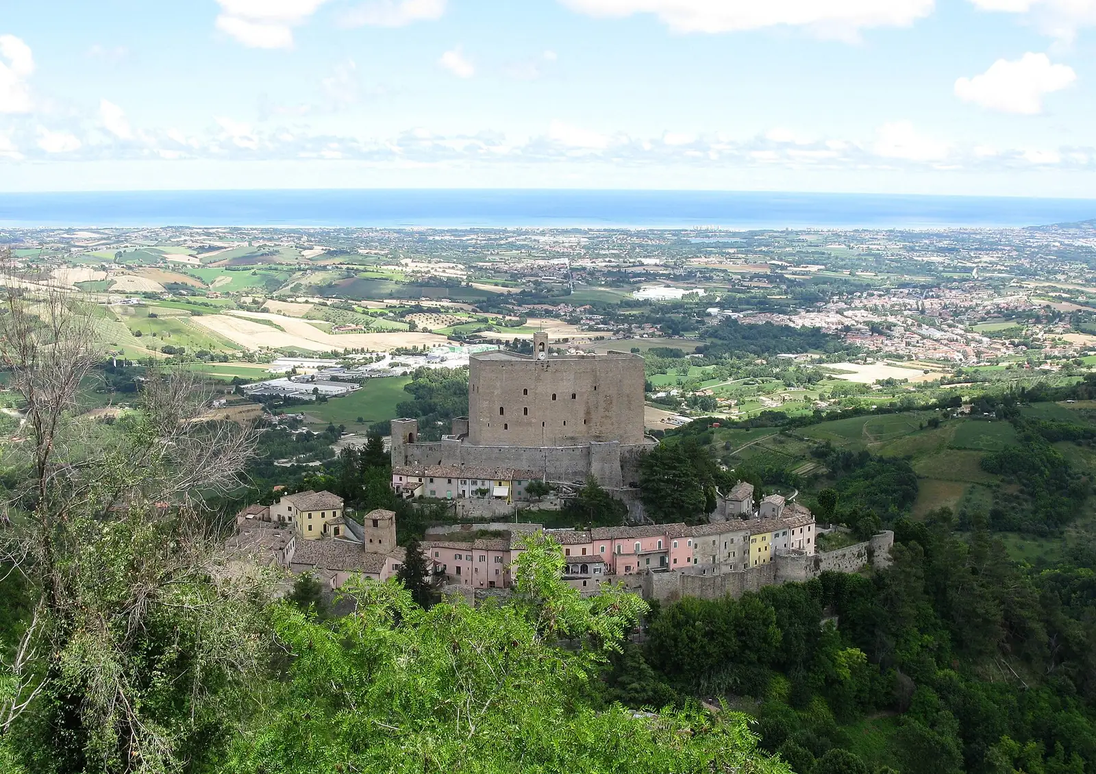 Montefiore Conca's fortress and colourful houses seen from above, with Valconca hills and the sea on the horizon