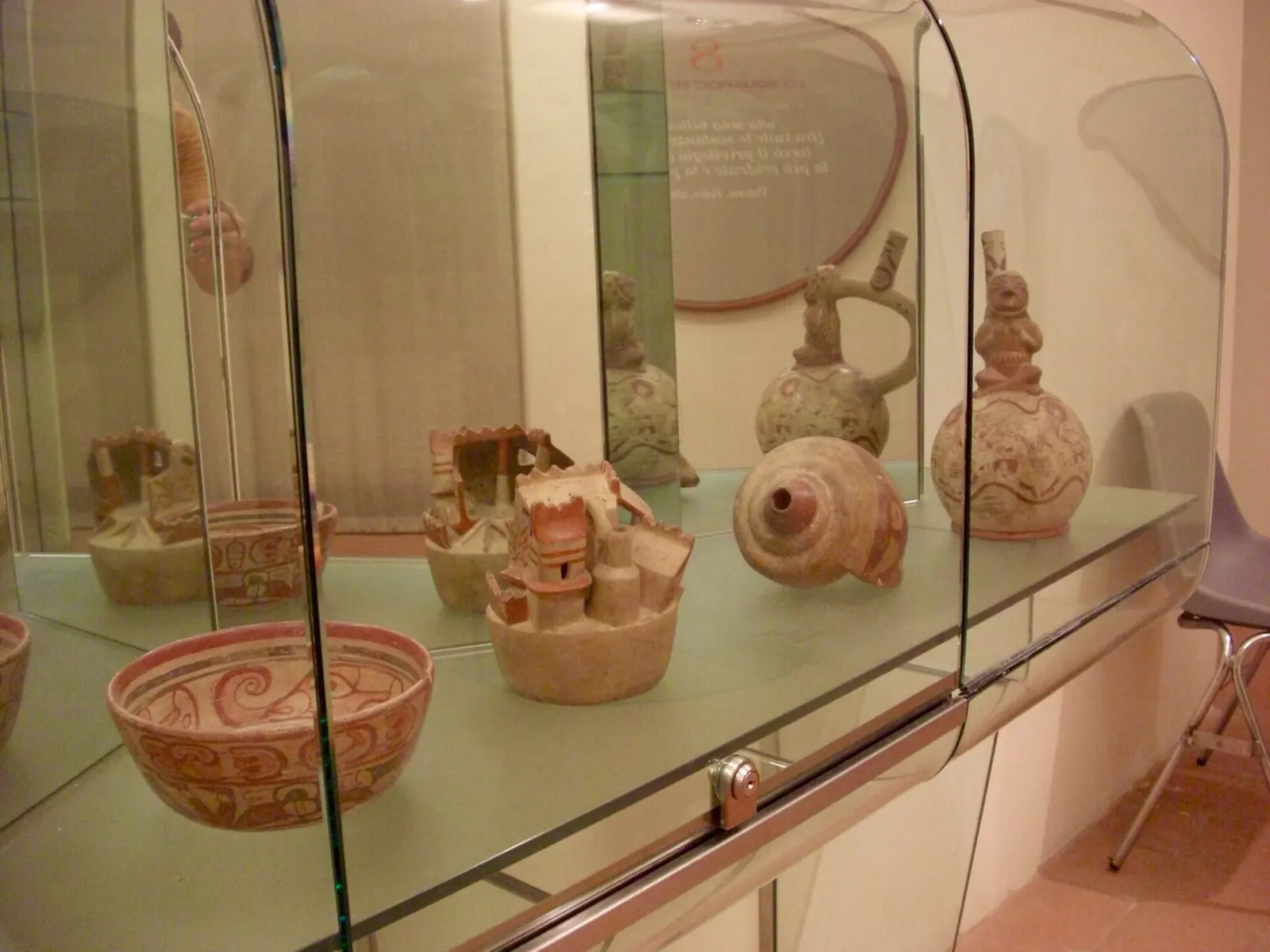 Verzierte Keramikschalen und -gefäße, eines mit einer sitzenden Figur, in einer gebogenen Vitrine des Museo degli Sguardi