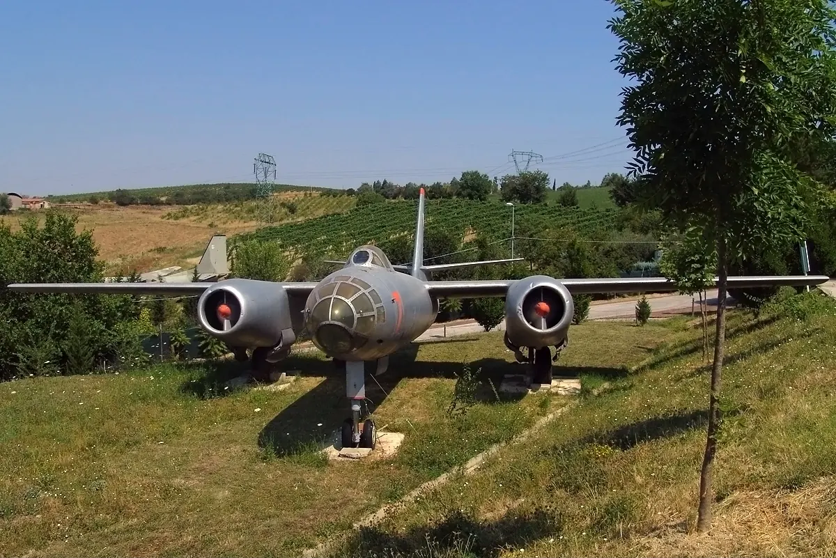 A grey twin-engine jet bomber with a glazed nose, displayed on a sloping lawn with vineyards behind