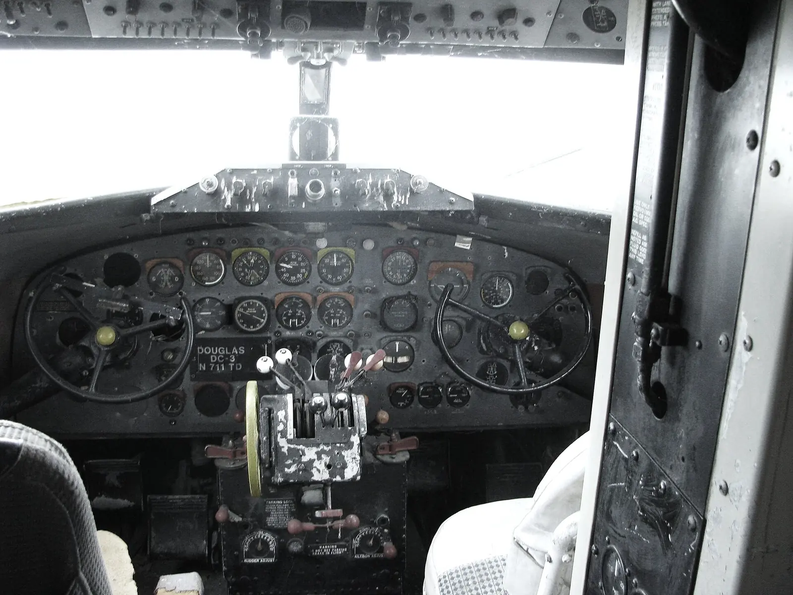 The cockpit of a Douglas DC-3, with two control wheels, an instrument-filled panel and throttles in the centre