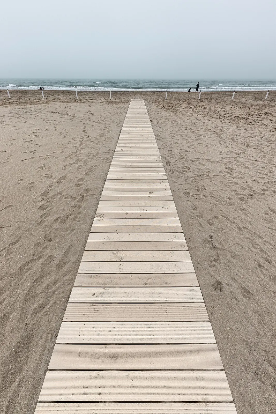A long walkway of pale boards crossing the sand to the sea at Milano Marittima on a foggy day