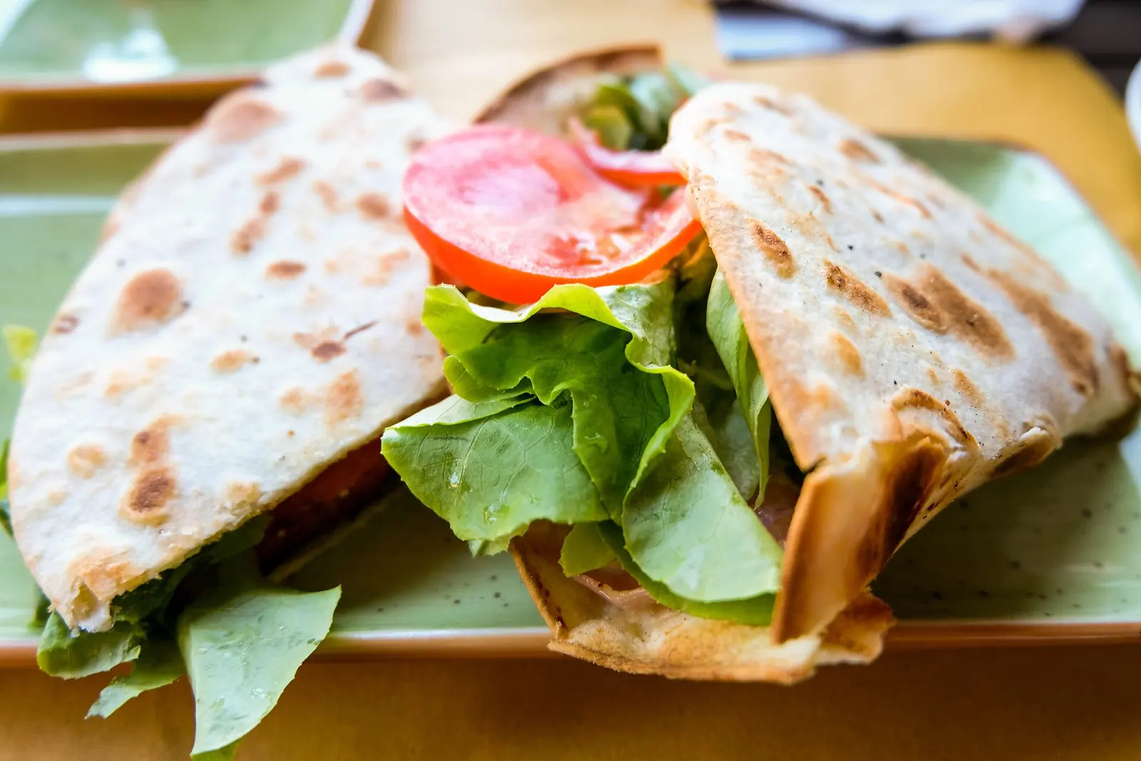 Una piadina ripiegata e farcita con insalata, pomodoro e prosciutto, servita su un piatto verde
