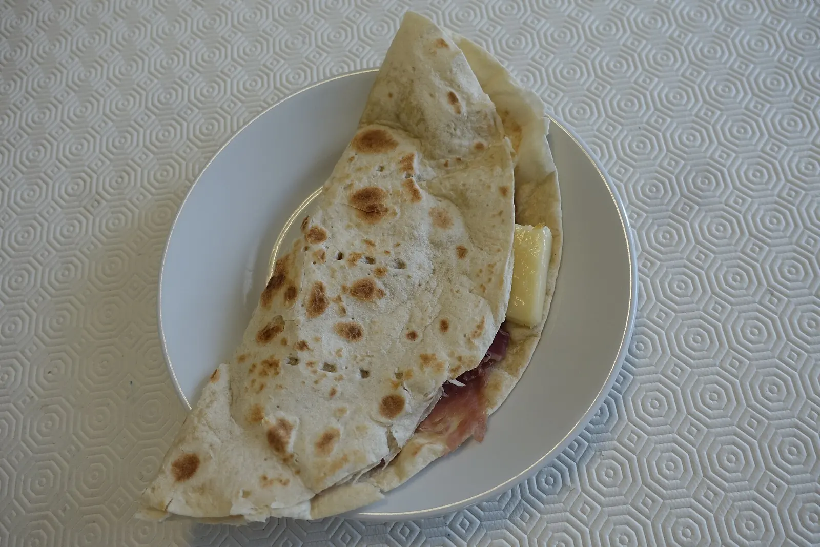 Una piadina chiusa a mezzaluna con prosciutto e formaggio, servita su un piatto bianco