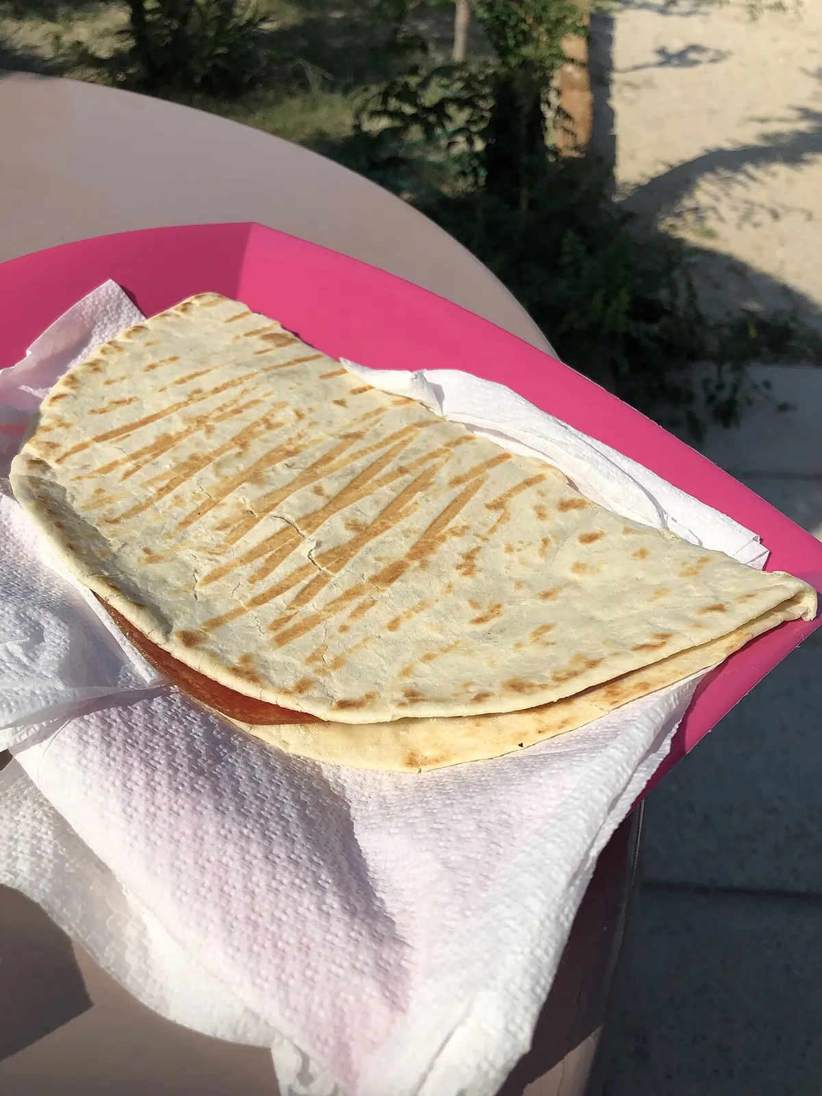 Una piadina ripiegata su un tovagliolo di carta e su un vassoio rosa, con i segni della piastra sulla sfoglia