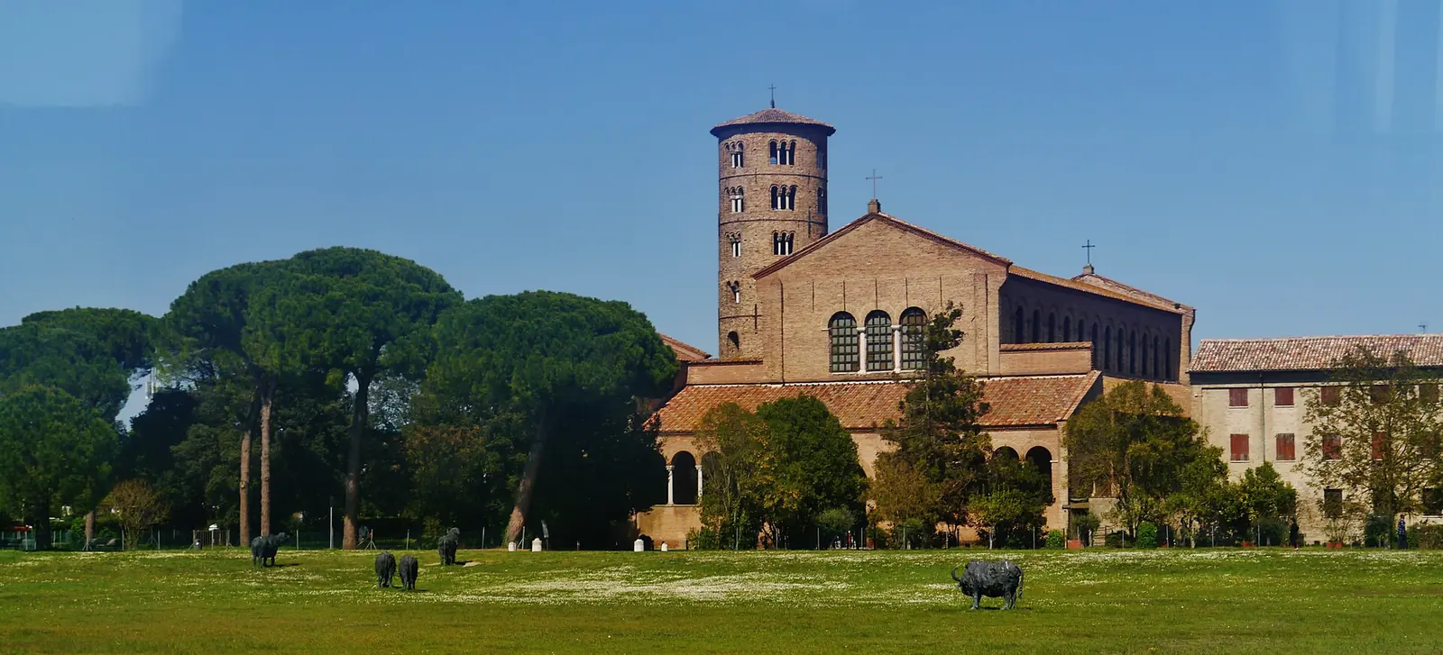 La basilica di Sant'Apollinare in Classe, con il campanile cilindrico in mattoni, fra i pini e un prato con sagome di animali