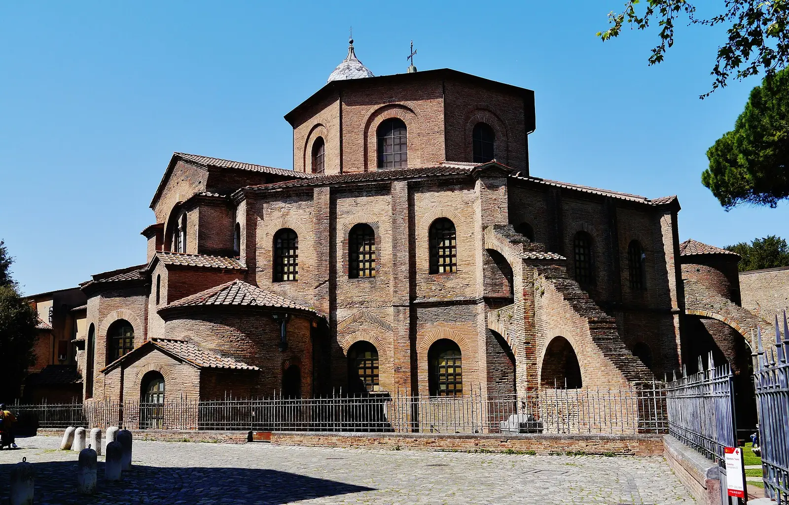The octagonal brick exterior of Basilica di San Vitale in Ravenna, behind railings