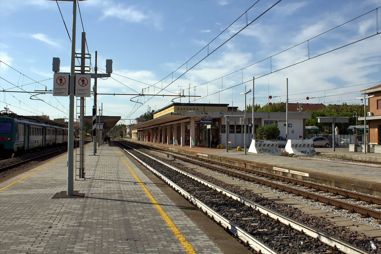 I binari e la banchina della stazione di Ravenna, con la pensilina sul fondo e un treno a sinistra