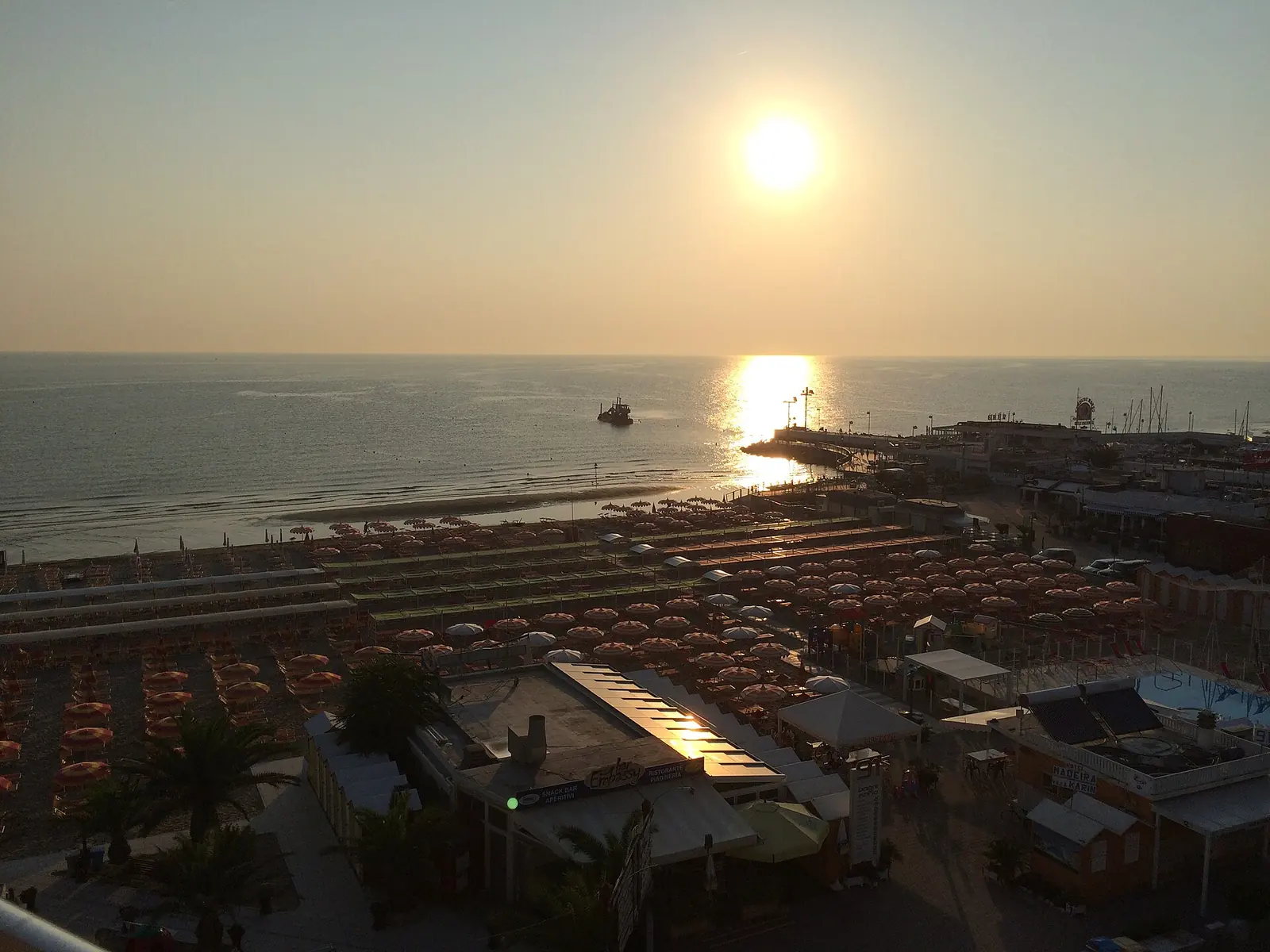 Sonnenaufgang über dem Meer in Riccione von oben über Sonnenschirmreihen und dem Hafenpier gesehen
