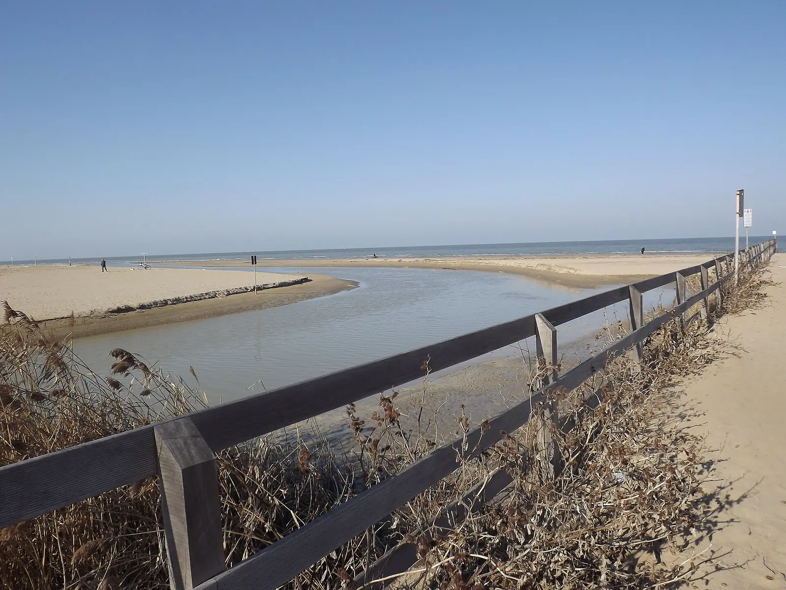 L'embouchure du Marano à Riccione : eau peu profonde sur le sable et clôture en bois au premier plan