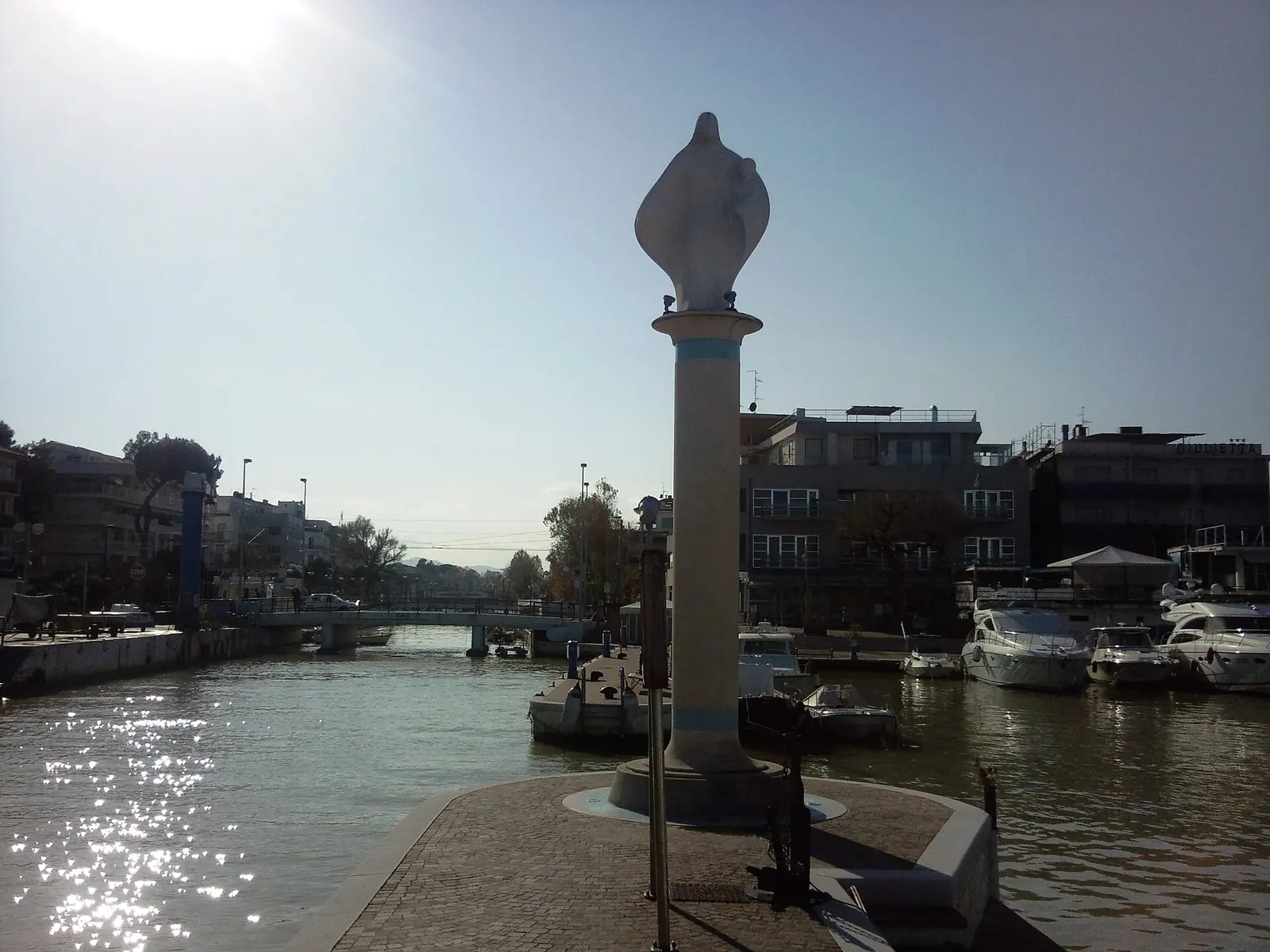 La colonne portant la statue de la Madonna del Mare au port-canal de Riccione, avec les bateaux amarrés le long des quais