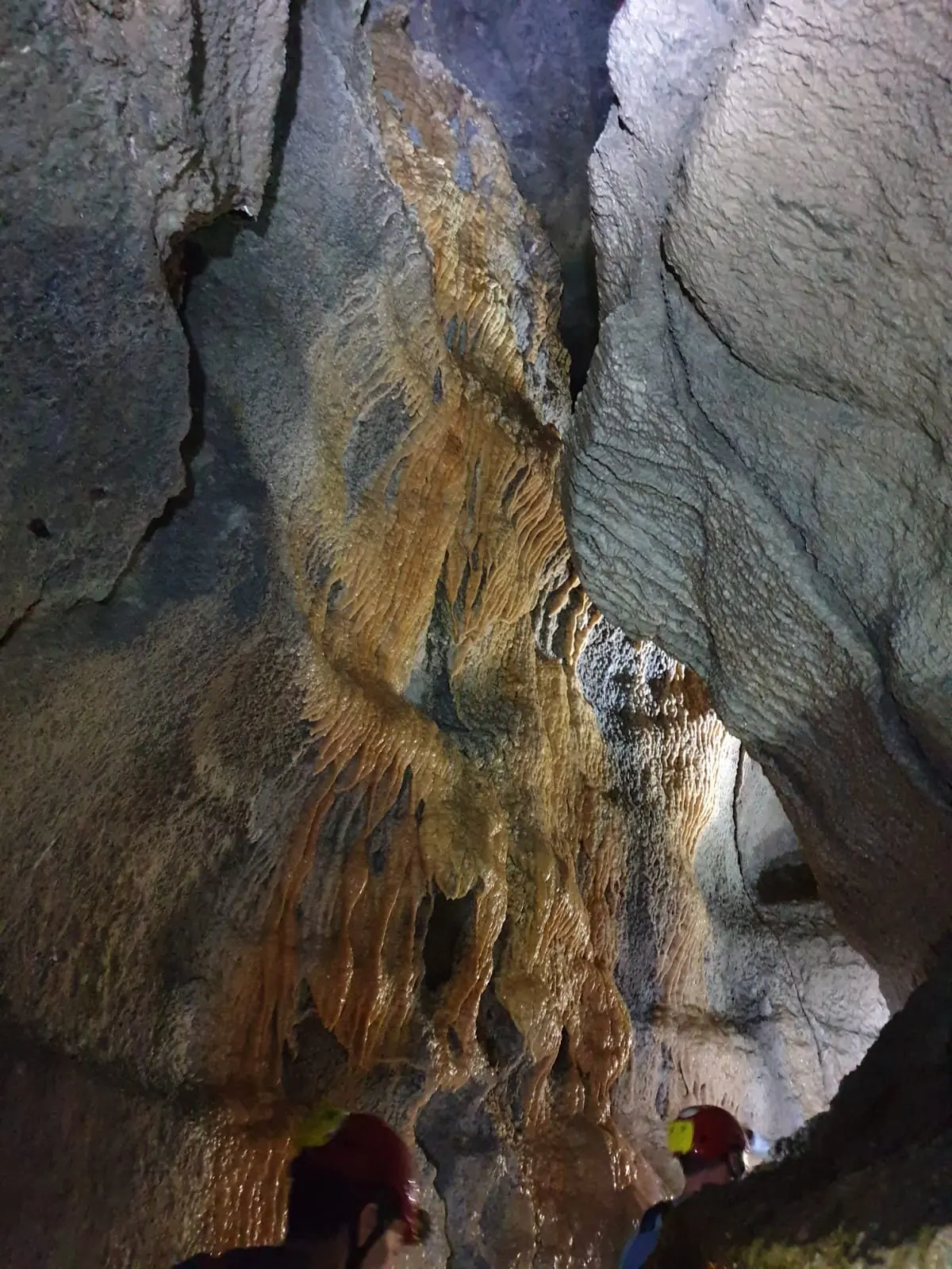 Una galleria della grotta di Onferno con concrezioni color ocra e due piccole sagome in basso